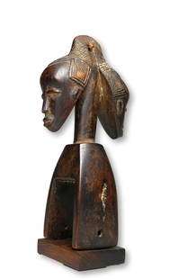 A Guro Janus Pulley: A very finely carved heddle pulley for a weaving loom, with a unusual Janus face and elaborate coiffure accented with some kaolin clay pigments. Guro peoples, Ivory Coast, West Africa. The Pulley meas