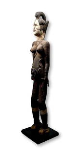 Igbo Alusi Guardian Figure: A tall carved wooden female effigy with elaborate coiffure, raised scar designs and a thick encrusted surface showing layers of applied organic material. Such idols are often placed on community shrin