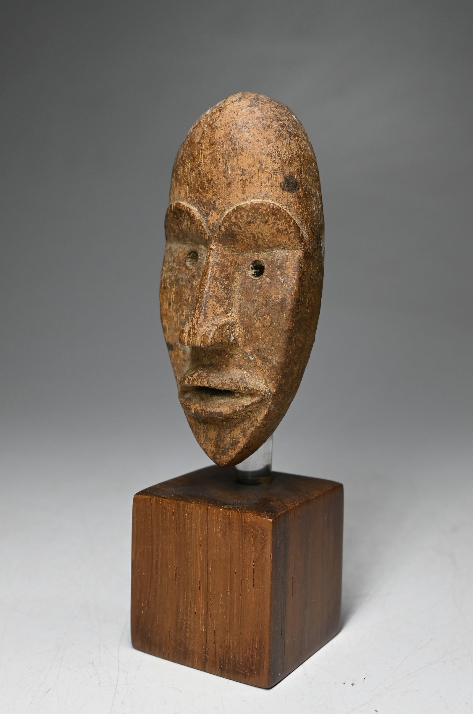 A Dan Poro Passport Mask: A carved wooden diminutive mask with blonde wood surface color and well handled patina, some evidence of offerings in the back of the mask. The Passport mask measures 3.5 inches, 5.5 inches tall on cu