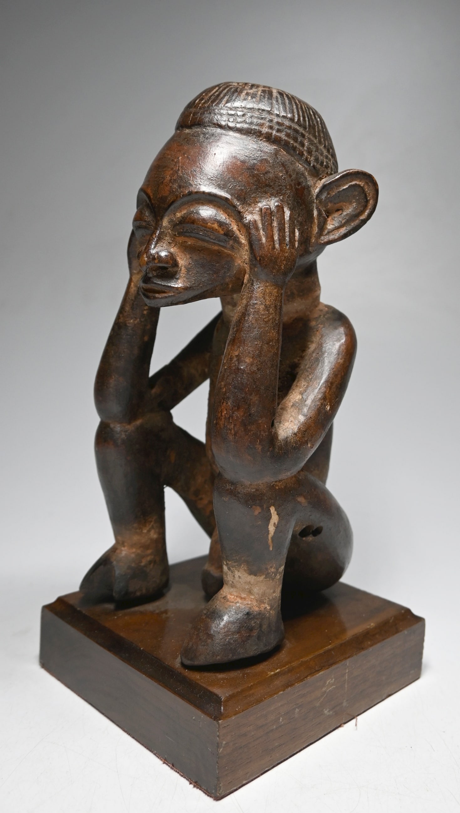 A Holo Male Ancestor Sculpture: A carved wooden male effigy with well handled and worn surface, carved coiffure and areas accented with mineral pigments. The sculpture appears to be a vintage to antique example. Holo peoples, DRC/ C