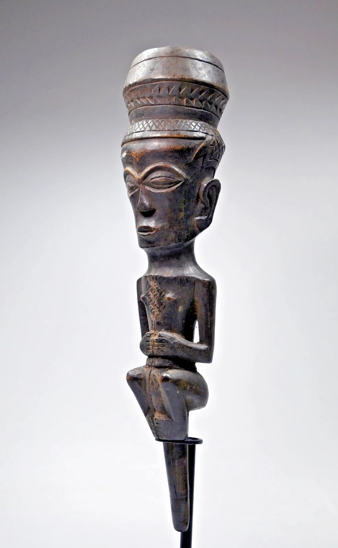 A Kuba Clyster or Funnel: A carved wooden funnel like form, which was meant to resemble a clyster, a ritual funnel, with an ancestor type figure and some elaborate carved geometric details. The original clyster funnels were me