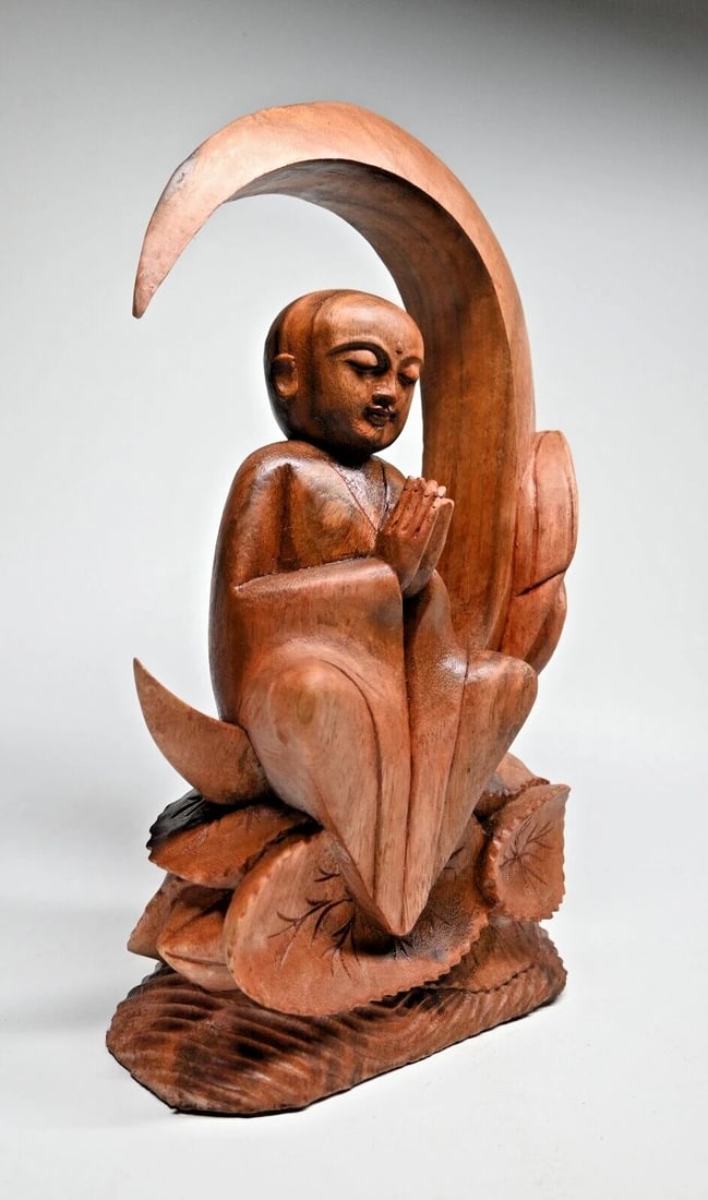 A Meditating Buddha on the Moon: A serene hand carved Suar wood Buddha shown meditating on a crescent moon and lotus flowers. The sculpture measures 16 inches tall x 10 inches wide. We purchase direct from the artist and her family,