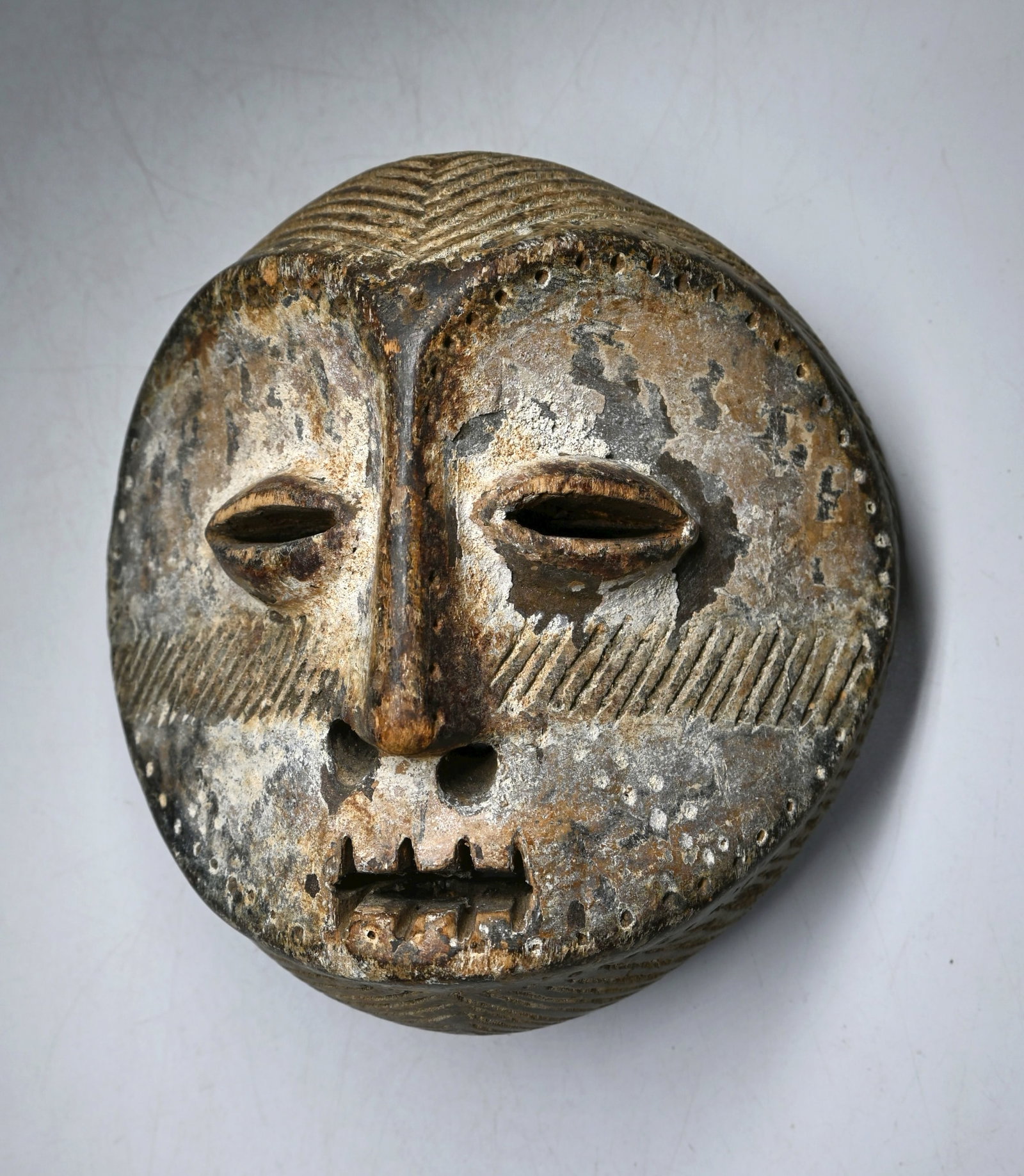 A Lega Mask with incised design: A charming carved wooden mask with kaolin clay pigments, incised tribal designs and linear designs around the outer edge of the mask. The mask measures 7 x 7.25 inches. Lega or related ethnic group, C