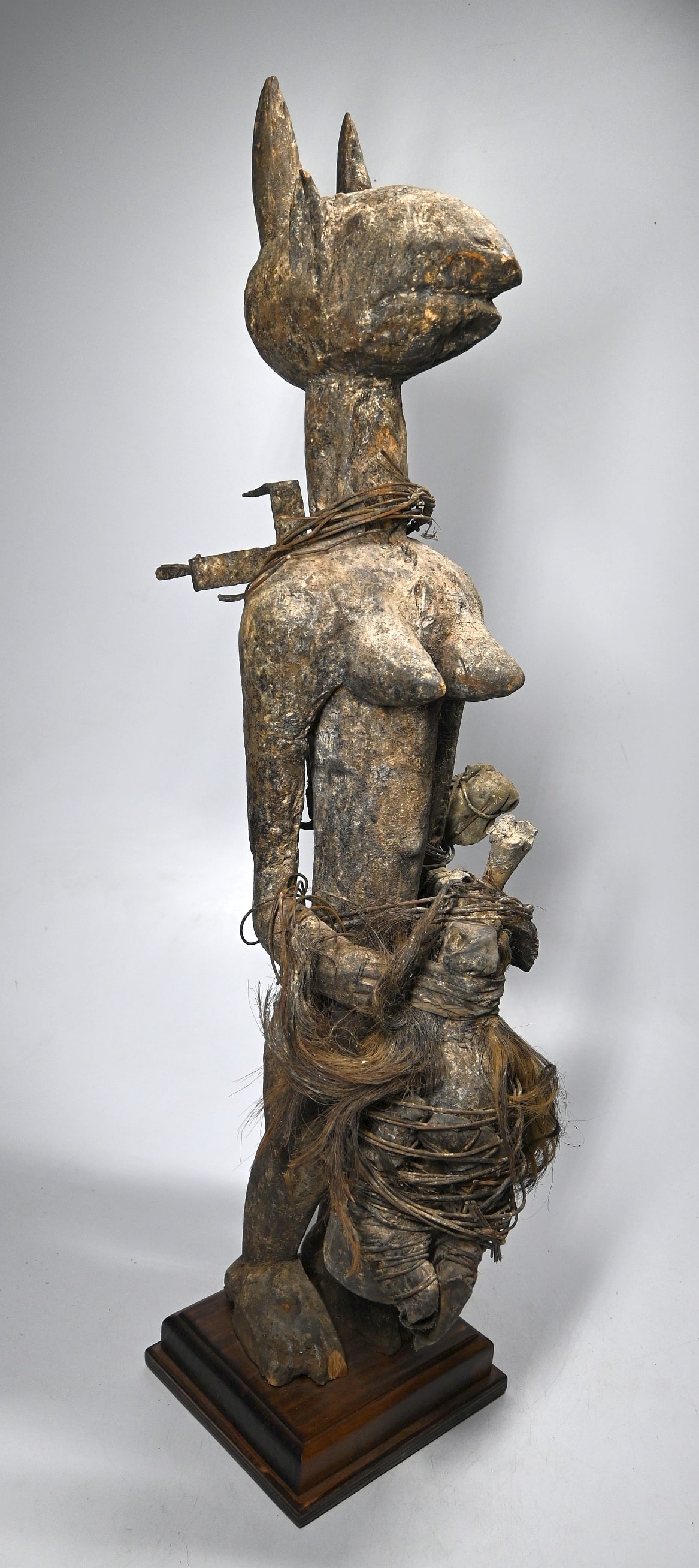 Large Fon Magic Shrine fetish: A tall carved female Vodoun fetish with animal attributes and many magic accoutrements including a large gin bottle sealed and adorned with animal hides, bone and shell attachments and magic bundles. 