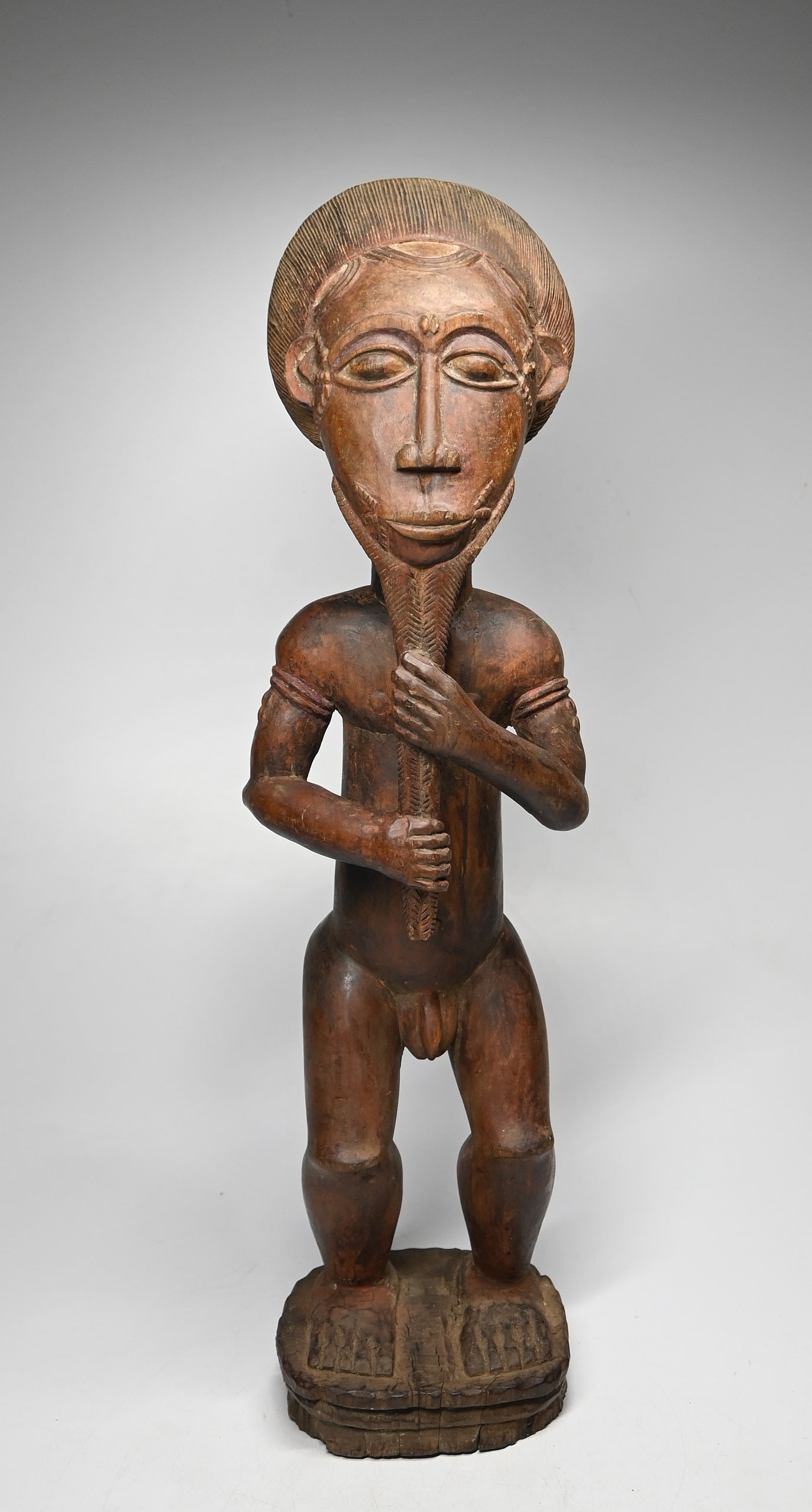 A Baule Male Sculpture: A finely carved male sculpture with a very finely carved coiffure, raised facial scars and a charming long braided beard which he holds as a sign of wisdom. Baule peoples, Ivory Coast, West Africa. Th