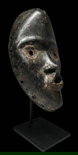 A Dan Mask Ex Charles Miller: A oval shaped carved wooden dance mask, likely from northern Ivory Coast due to the shape, with metal work around the eyes and with hand drilled square and round attachment holes around the perimeter.