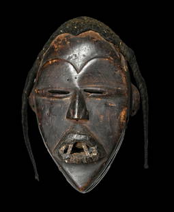 A Dan Mask Ex Bordogna: A Carved wooden mask, likely a deangle mask with attached woven grass fiber coiffure, inset metal teeth , slit eyes and incised linear designs. The mask measures 8.25 x 5 inches. Dan Peoples, Ivory Co