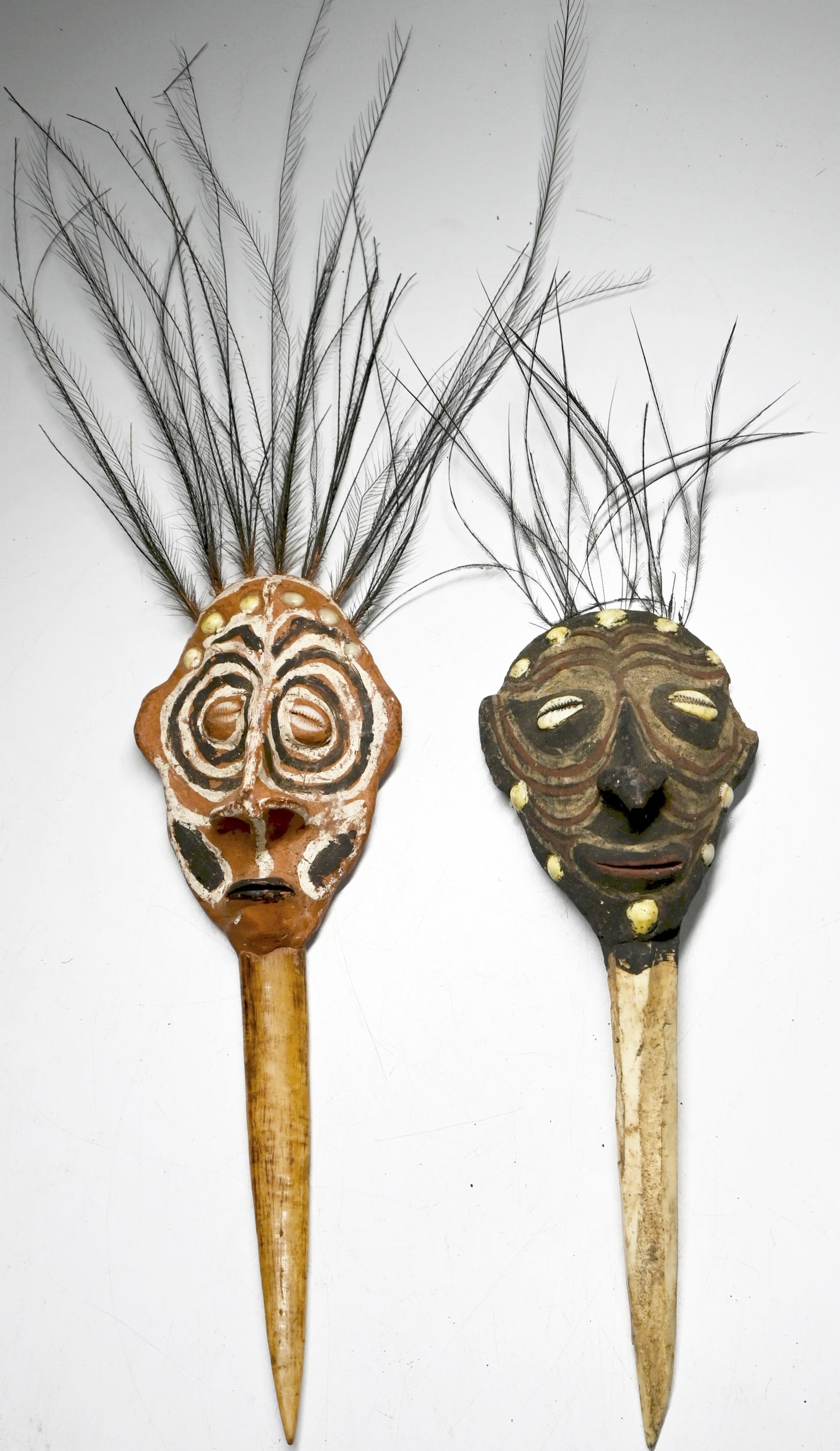 Pair of Latmul Bone Daggers: This lot contains 2 cassowary bone daggers with over modeled clay faces, painted and embellished with cowrie shell eyes and cassowary feathers. The daggers are sometimes referred to as payback daggers