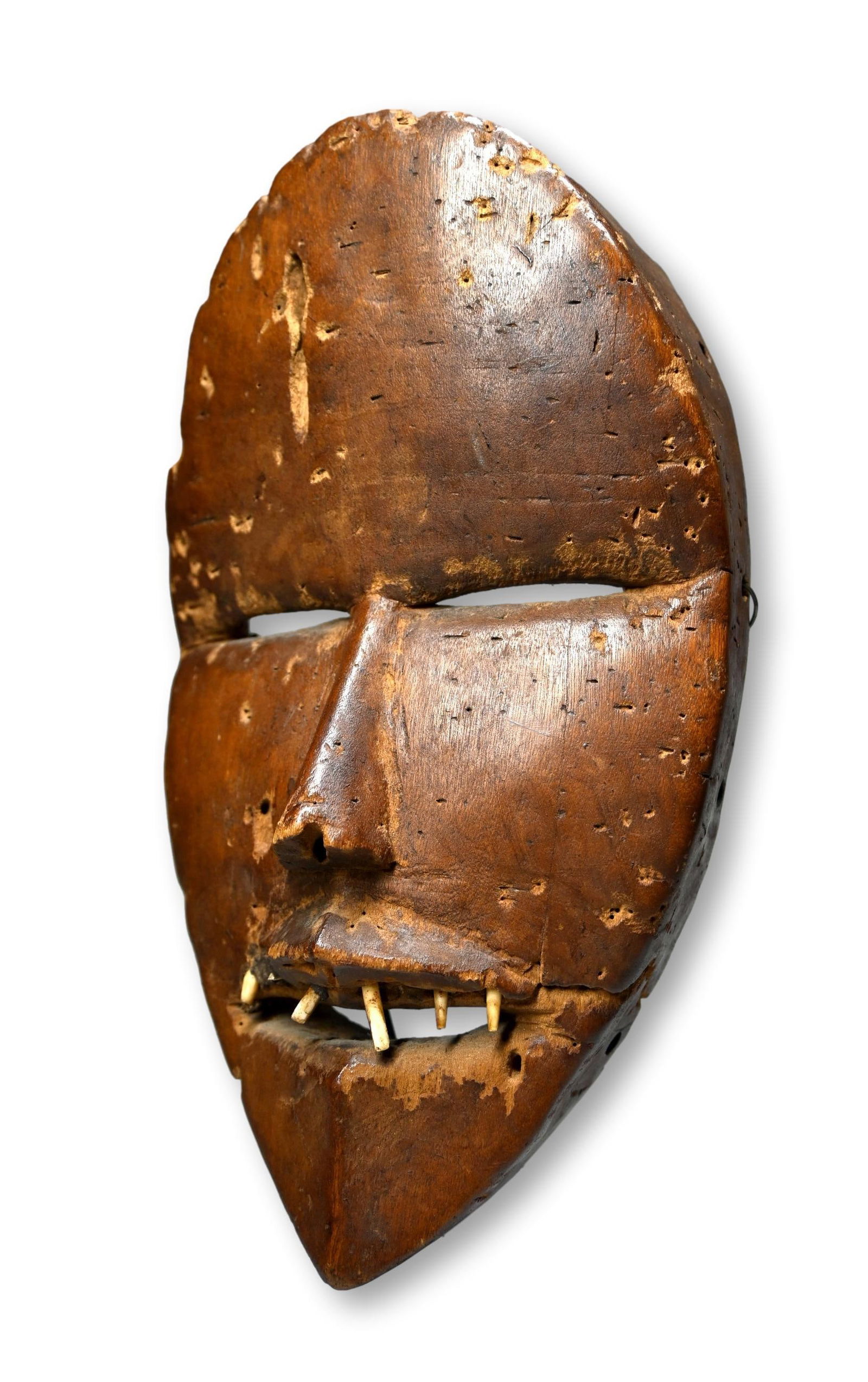 A Dan African mask: Carved wood rendered in classic style, possibly a Tanka Gle mask with inset animal teeth and a overall well handled and worn surface indicating years of ritual use. The mask measures 10 x 6 inches. Th