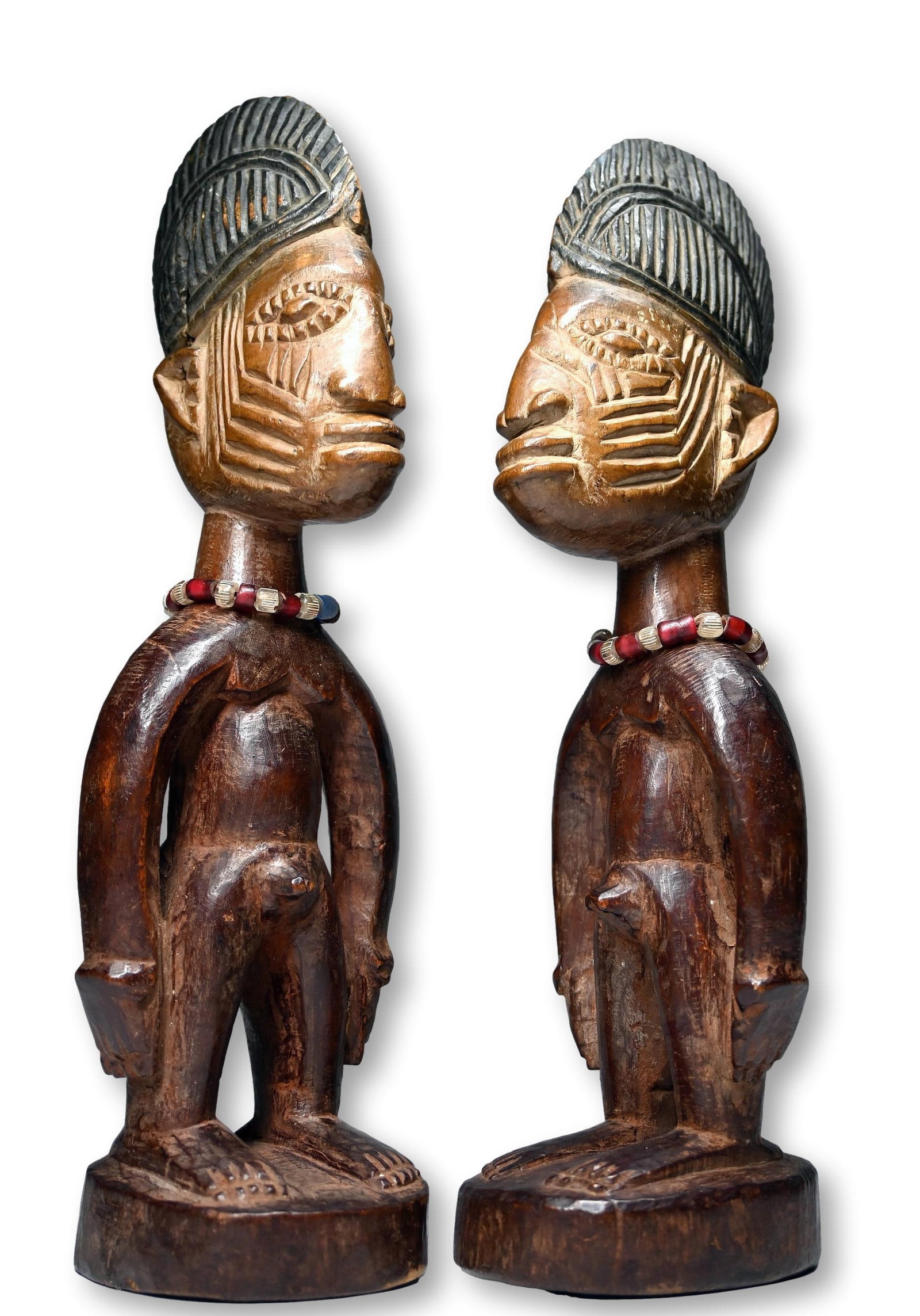 A Pair of Ibeji Twin Cult Sculptures: A carved wooden male and female pair of Ibeji sculpture with deep facial scars, and well carved coiffure and a well handled surface patina. Note how both of the faces were washed and cleaned. Ibeji Tw