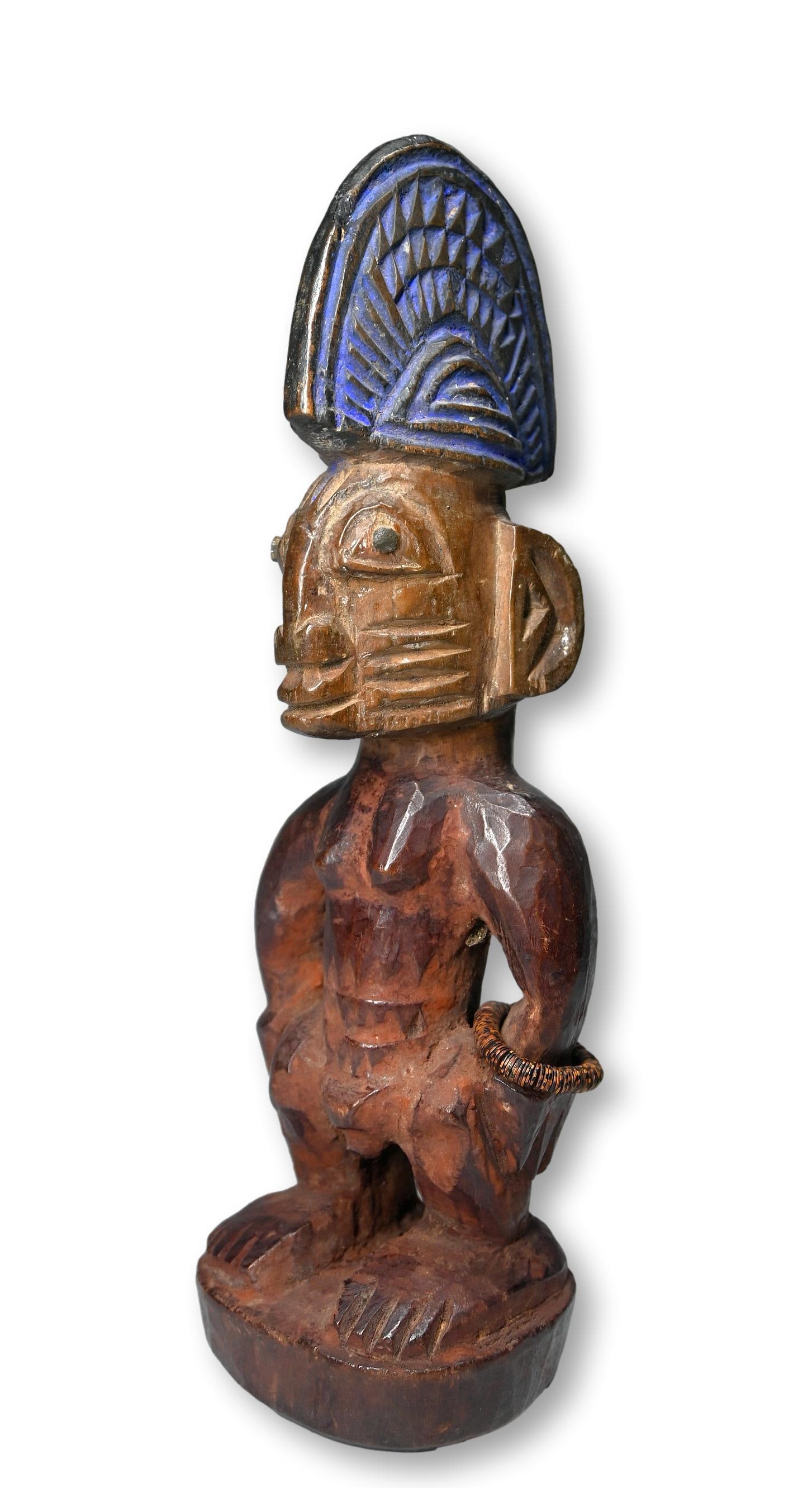A Female Ibeji Twin Idol from Ogbomosho: A carved wooden female twin sculpture with deep facial scars, a large carved coiffure with strong blue pigments and a well handled surface patina. Ibeji Twin sculptures are created by the Yoruba peopl