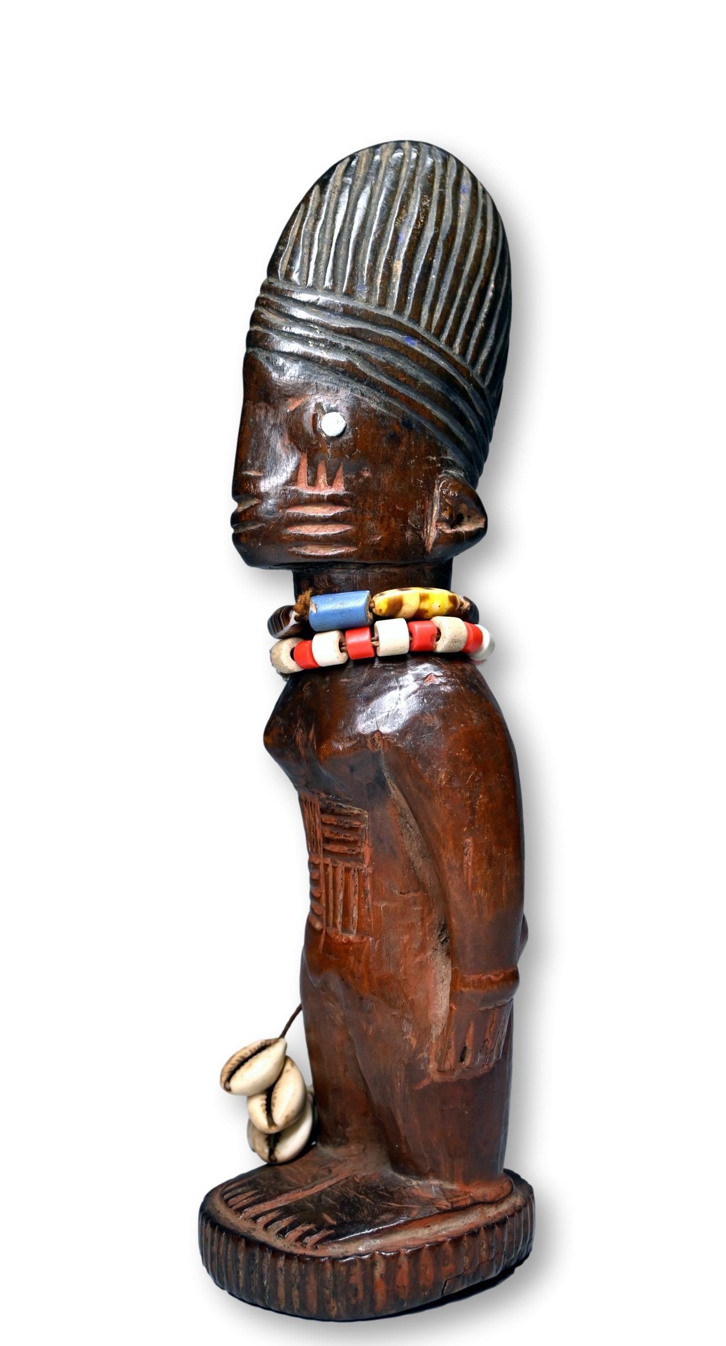 Scarce Ibeji from the Yoruba Owu of Ibadan Village: A finely carved wooden female twin sculpture with facial scars, inset nails for eyes, a tall detailed coiffure and a very well handled surface patina. Ibeji Twin sculptures are created by the Yoruba p