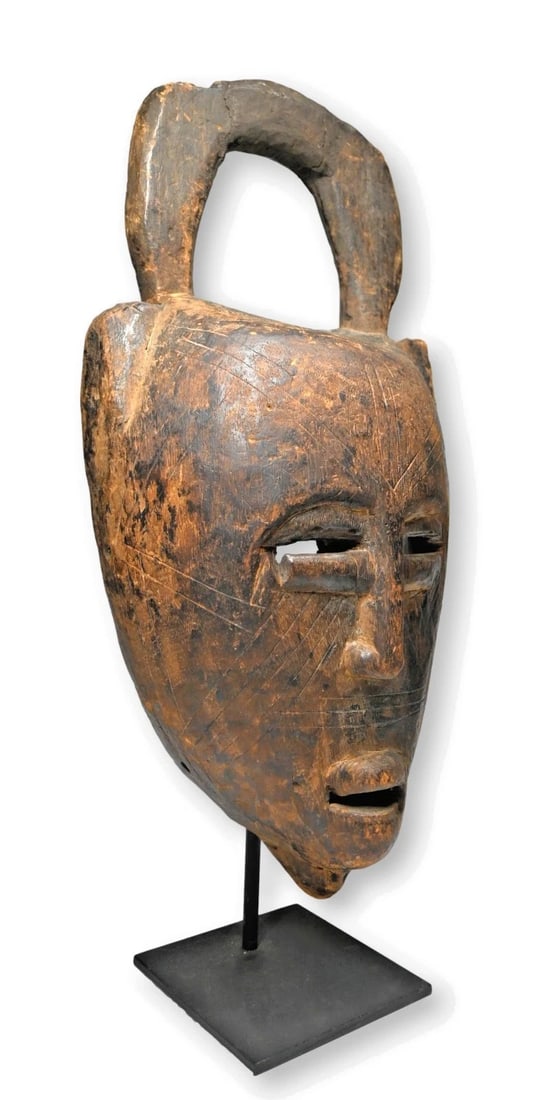 Old Bamana Mask: A carved wooden dance mask with a stylized face with incised linear scar like designs and a top arch like finial,. The mask showing wear on the interior and obvious weathering on the exterior, restora