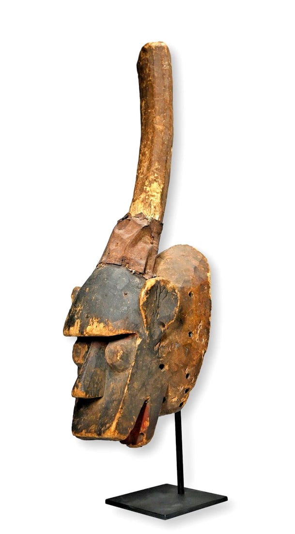 A Baule African Mask: A carved wood and painted well used ceremonial mask with raised central post like finial that at one time was adorned with feathers and animal hide, now worn away. The mask has an overall well worn su