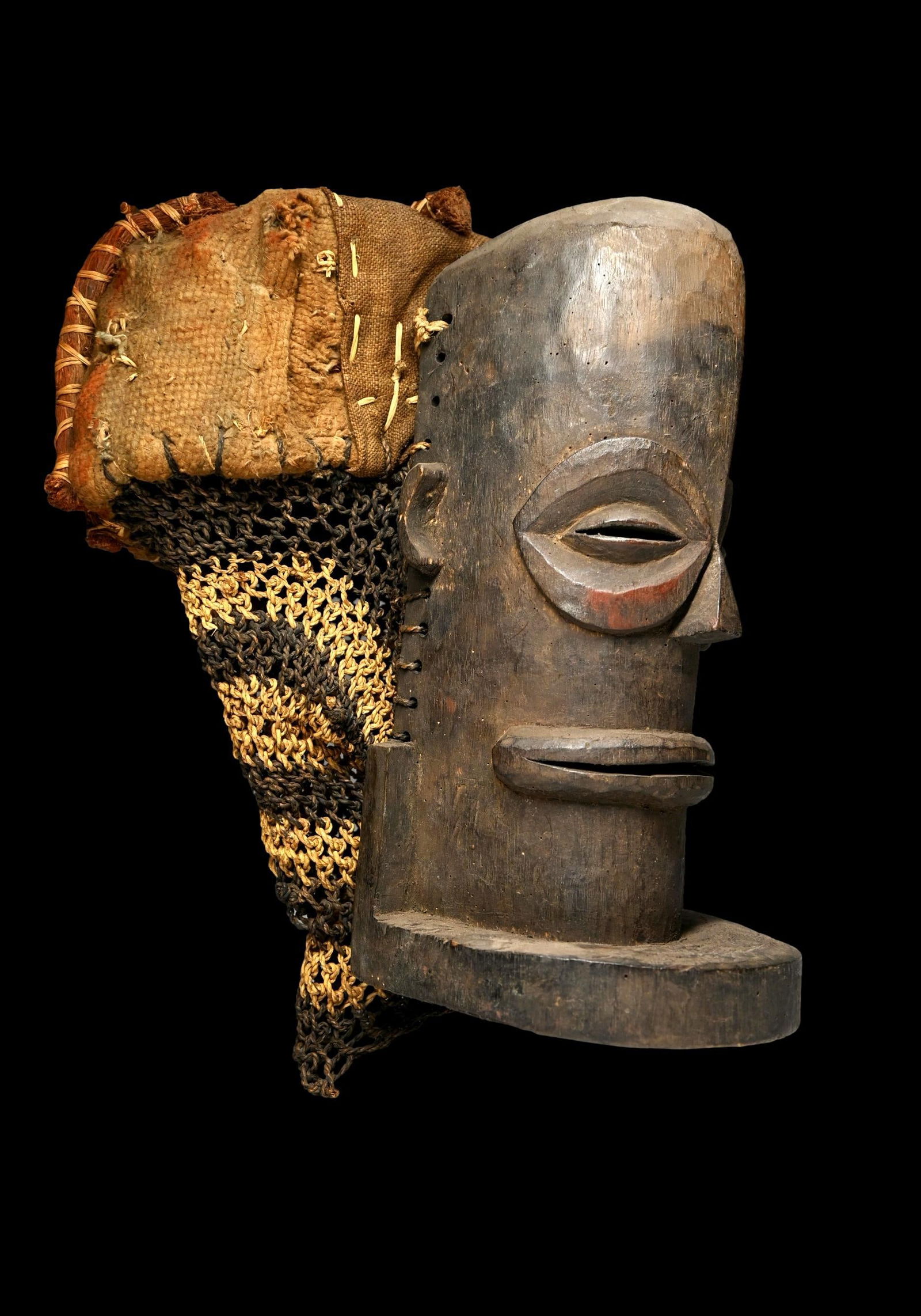 A Chokwe Cihongo Male Mask: A Chokwe Cihongo Male ceremonial mask, Angola, Africa. Carved wood with elongated and exaggerated features, adorned with plant fiber and woven rope headdress. Chihongo represents a male spirit and ref