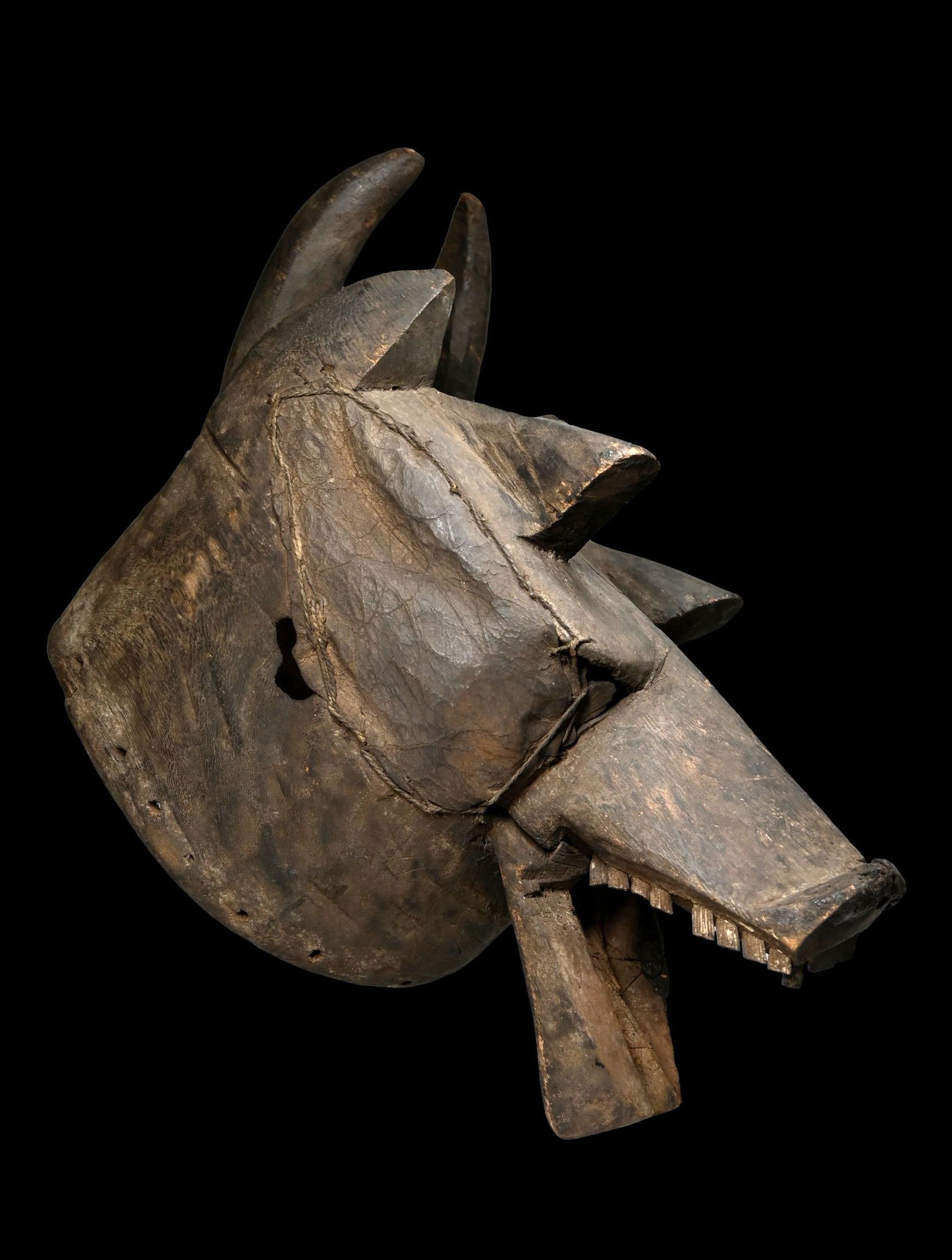 A Mambila Helmet mask: A very ART BRUT style carved wooden helmet mask with aggressive open mouth, inset wooden teeth and embellished with stretched animal hide over some of the holes in the mask, perhaps as a form of repai