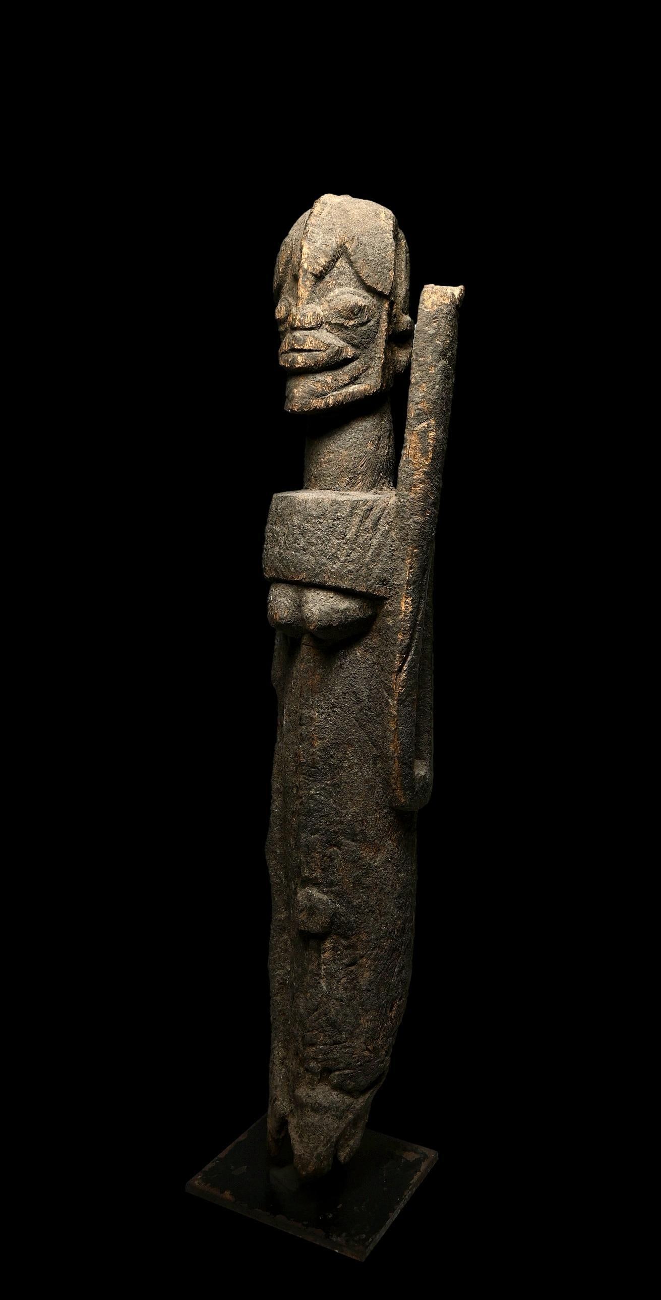 A Dogon Sculpture: A tall weathered sculpture of a female ancestor, possibly a Nommo cult idol, with arm raised to the heavens and with a encrusted surface, and eroded torso suggesting great age. Dogon sculptures with o