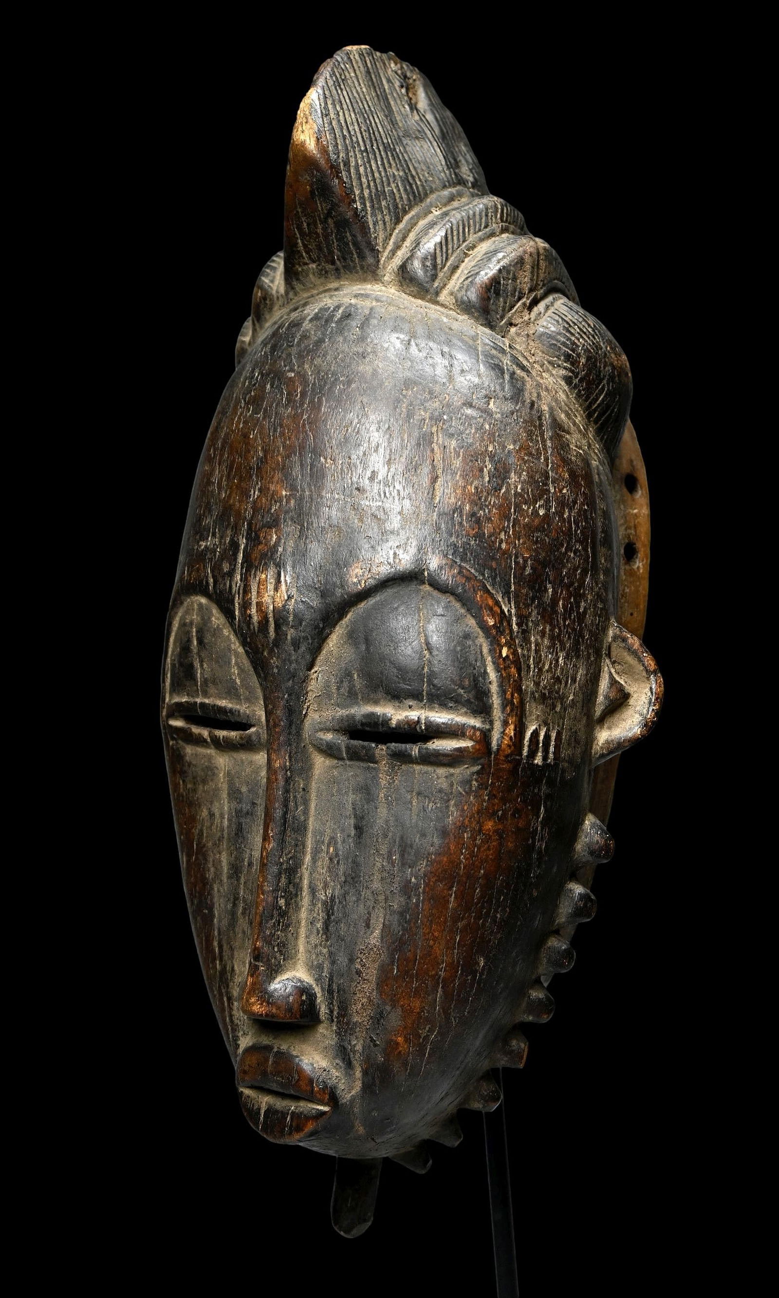 A Baule Portrait Mask: Carved from a dense wood in classic form with finely carved facial features, this mask known as mblo, was danced during dramatic skits and solo dances, this mask is an idealized representation of the