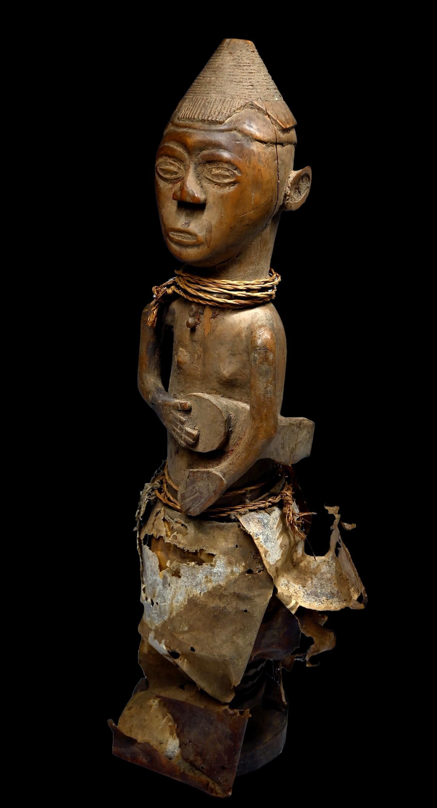A Kuba Musician Sculpture: A carved wooden sculpture opf a musician, a Drummer adorned with a traditional mens hat and at one time adorned with various animal hides, now all decayed. A very old example. Kuba peoples, Congo, cen