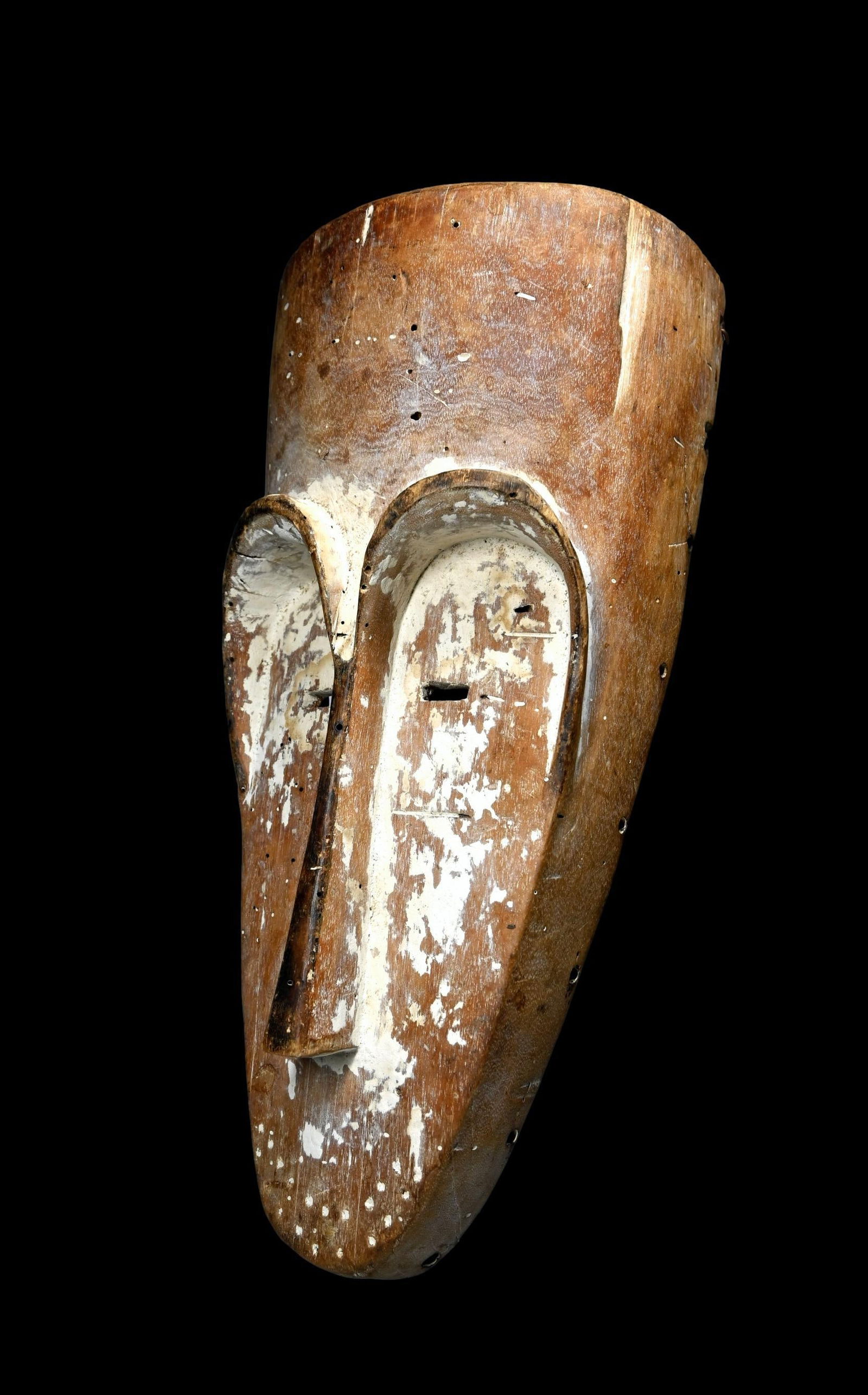 A Fang Mask: A carved wooden elongated mask with classic treatment to the face and central nose bridge and raised brow, remains of kaolin clay pigments on the mask face, weathered surface. The mask measures 17 x 8