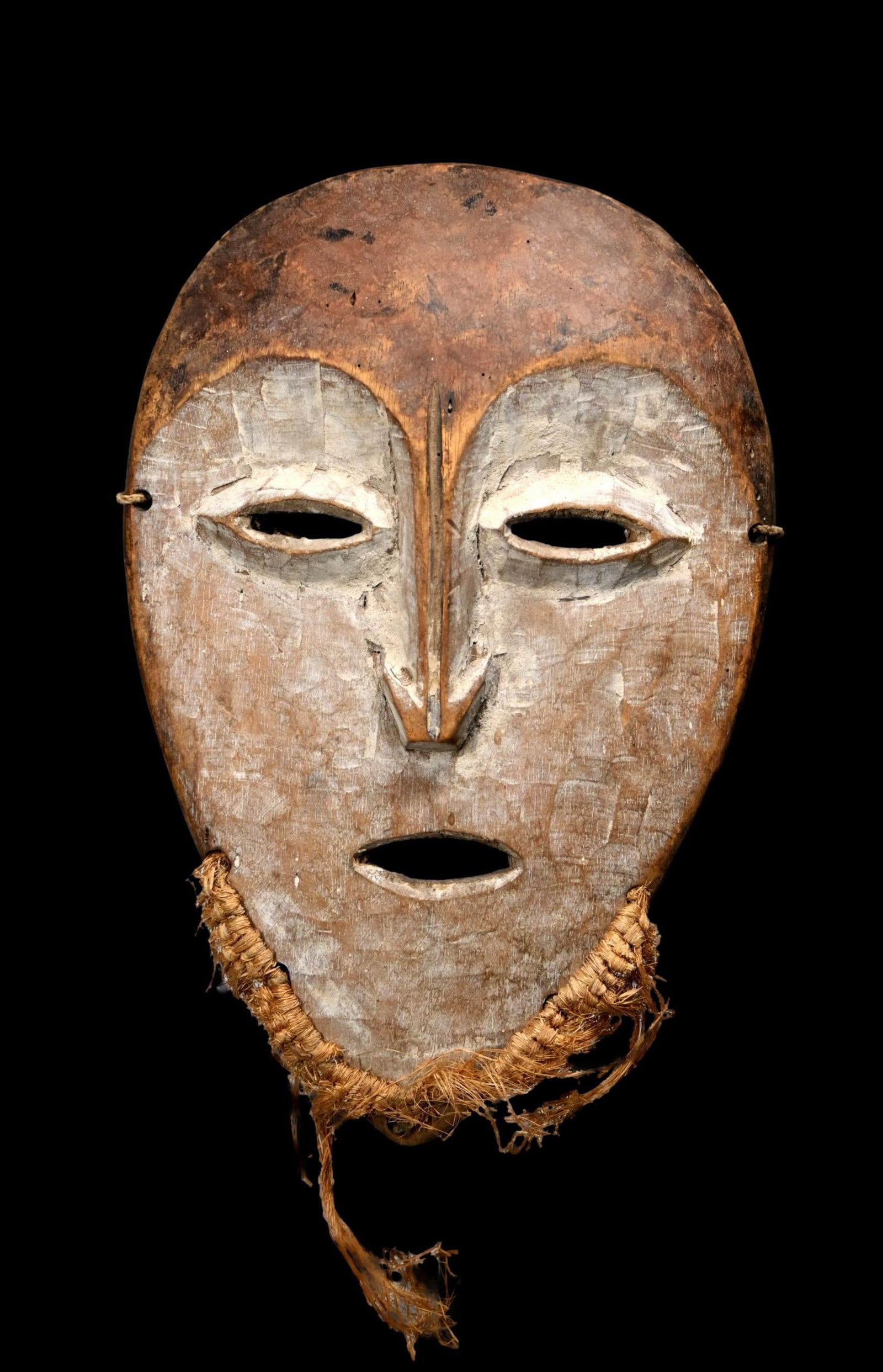 A Lega Mask: A carved wooden face mask painted with kaolin clay mineral pigments and with classic rounded face and almond shaped eyes created by the Bwami society for ceremonial use. This mask measures 12 x 8 inch