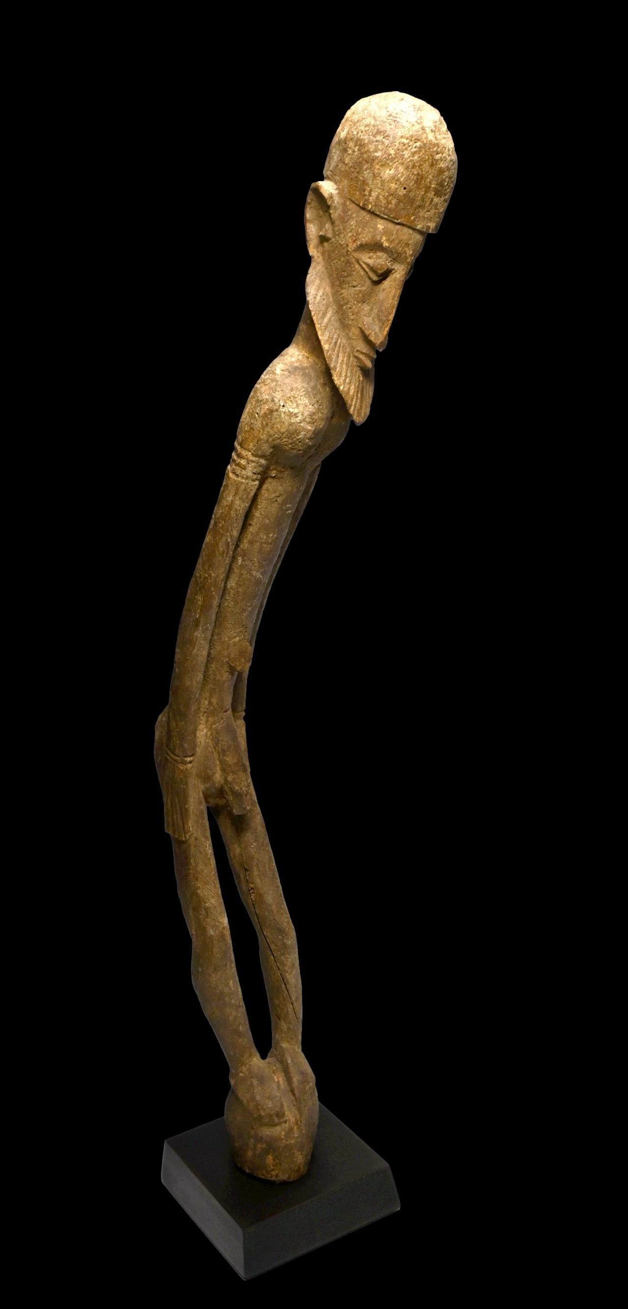 Elongated and Twisted Dogon Elder Sculpture: A wonderfully twisted carved wooden elder sculpture with weathered surface and some incised designs. Dogon peoples, Mali, Africa. The sculpture measures 38 inches tall on custom display stand. Provena