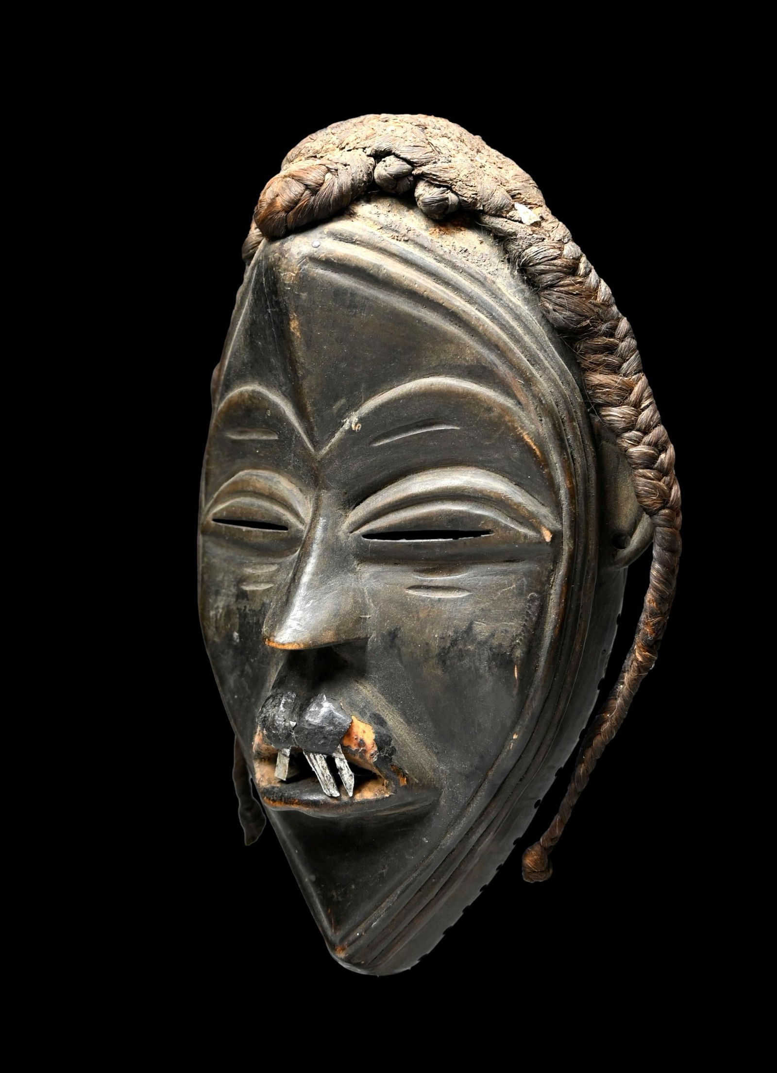 A Dan African mask: A finely carved older mask with inset metal teeth and woven grass coiffure incised linear designs. The mask has had restoration to the mouth and lip, clearly visible. Otherwise a great old example. Da
