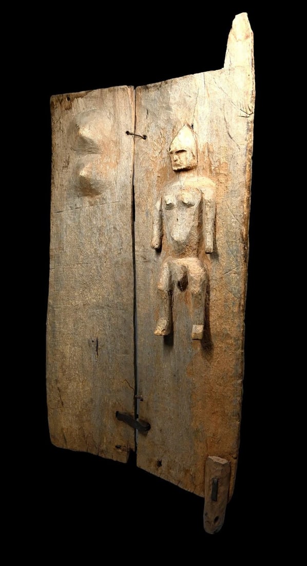 A Dogon Door: A large old carved wooden granary door with female effigy on front and the carved breasts symbolizing fertility. Dogon Peoples, Mali, West Africa. The door made from two panels secured by iron staples