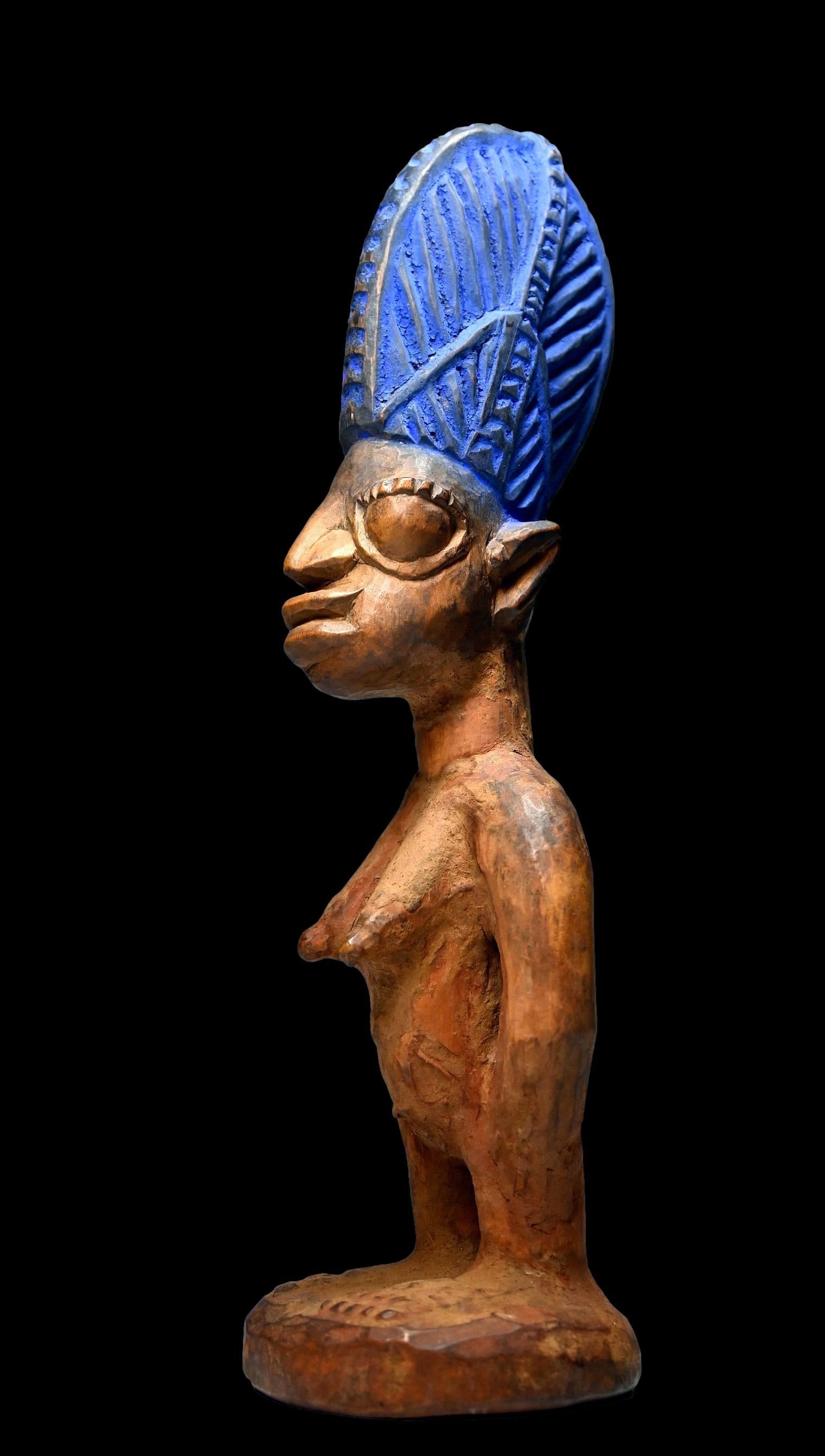 A Yoruba Ibeji Twin Effigy: A carved wooden female twin sculpture with a tall carved coiffure dyed blue and a well handled surface patina. Ibeji Twin sculptures are created by the Yoruba peoples of Nigeria , West Africa, who