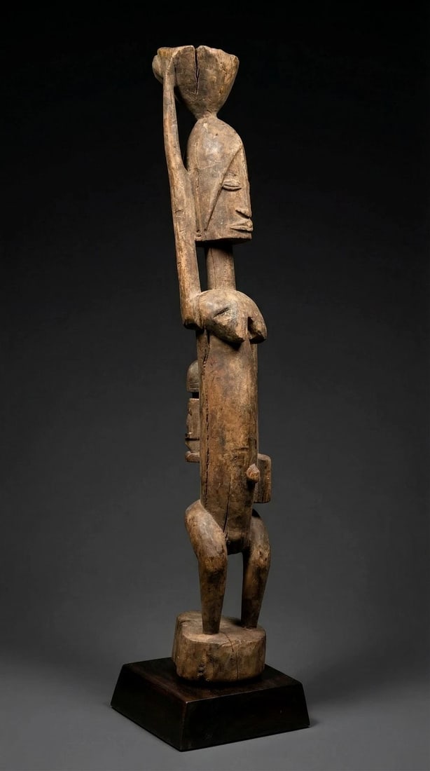 A Dogon Female Sculpture: A sculpture of a stylized female ancestor shown carrying a burden / vessel on her head and with a child on her back, with well weathered features and a classical form.Dogon "Seno" or "Senu" sculptures