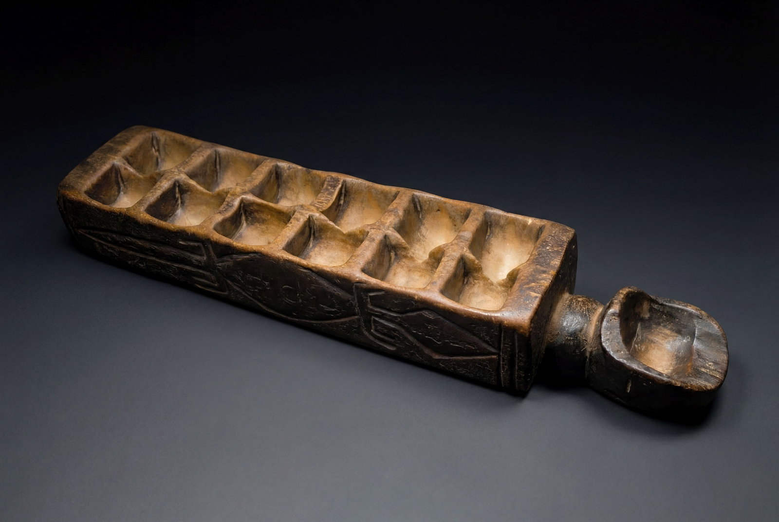 Dan Kran Mancala Game Baltimore Museum of Art 1968: A very well used, likely 19th century wooden game board with incised linear designs and obvious age and field use. The wooden game measures 21 inches long. Dan peoples, Kran Ethnic group under the Dan