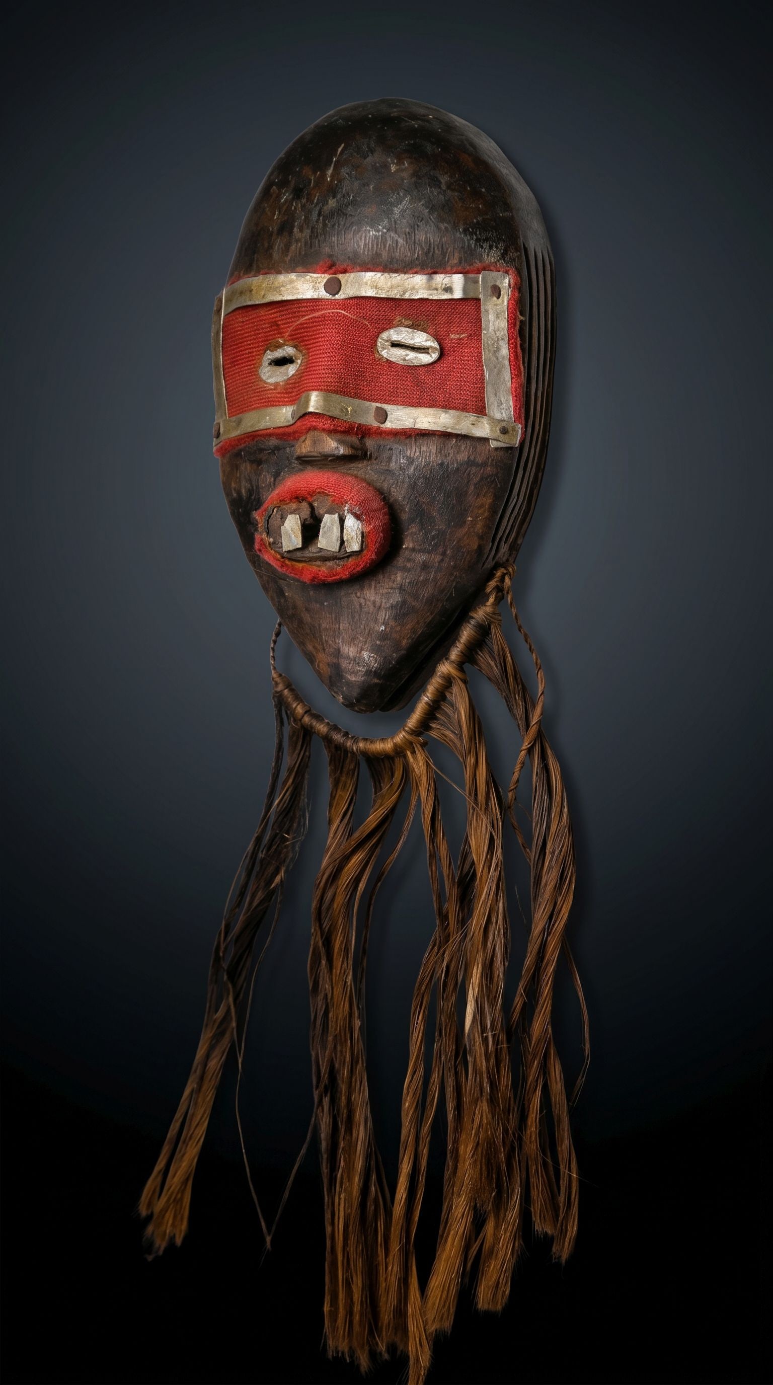 A Dan Mano Passport Mask: A Carved wooden mask accented with strips of aluminum, incised linear designs and red felt. Dan Mano peoples, Ivory Coast / Liberia, West Africa. The mask measures 5.5 x 3.25 inches, with beard it mea