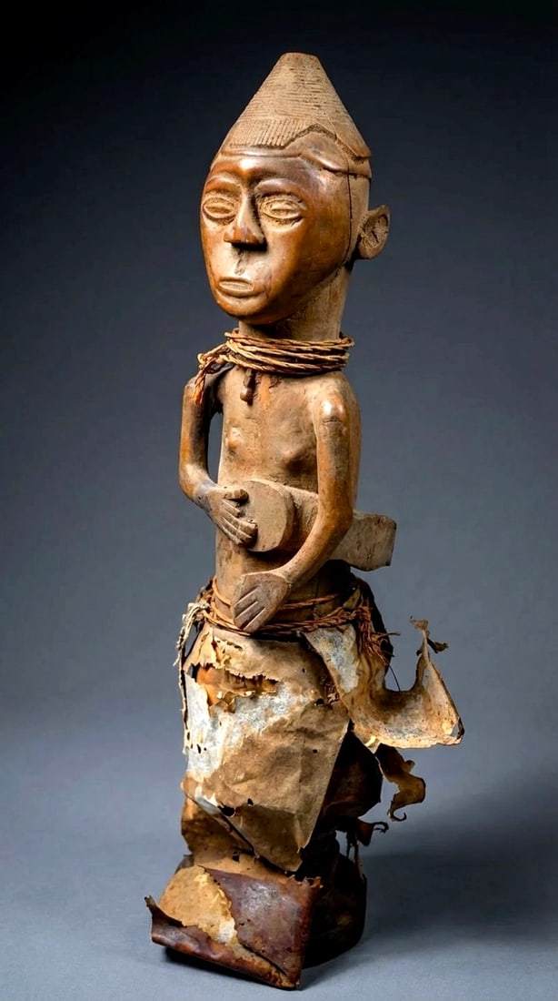 A Kuba Sculpture of a Drummer Ex Stirner Collection: An old carved wooden sculpture of a musician, a Drummer adorned with a traditional men's hat and at one time adorned with various animal hides, now all decayed. A very old example. Kuba peoples, Congo