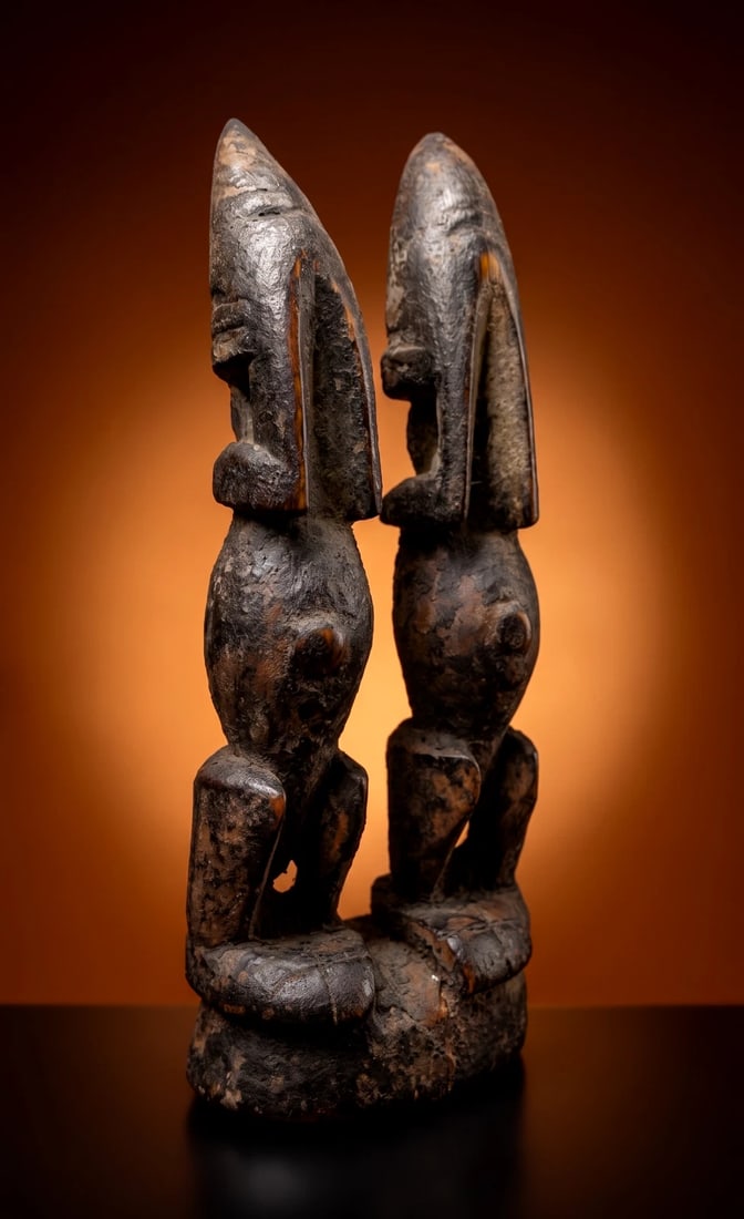 A Dogon Mourning Couple Ex Pearson Collection: A sculpture of an ancestor couple as Djougou Sirou, in mourning or shame for violating the earth and sewing forbidden seeds which brings the aspect of death to mankind. The sculpture is heavily encrus
