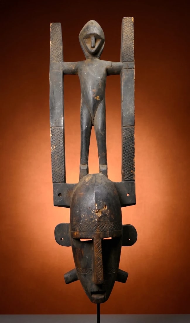 A Bamana Ntomo Mask: A carved wooden dance mask with a highly stylized face and form with a anthropomorphic figure on top, the mask has a unusual style with incised linear scar like designs. The Ntomo Society is the first