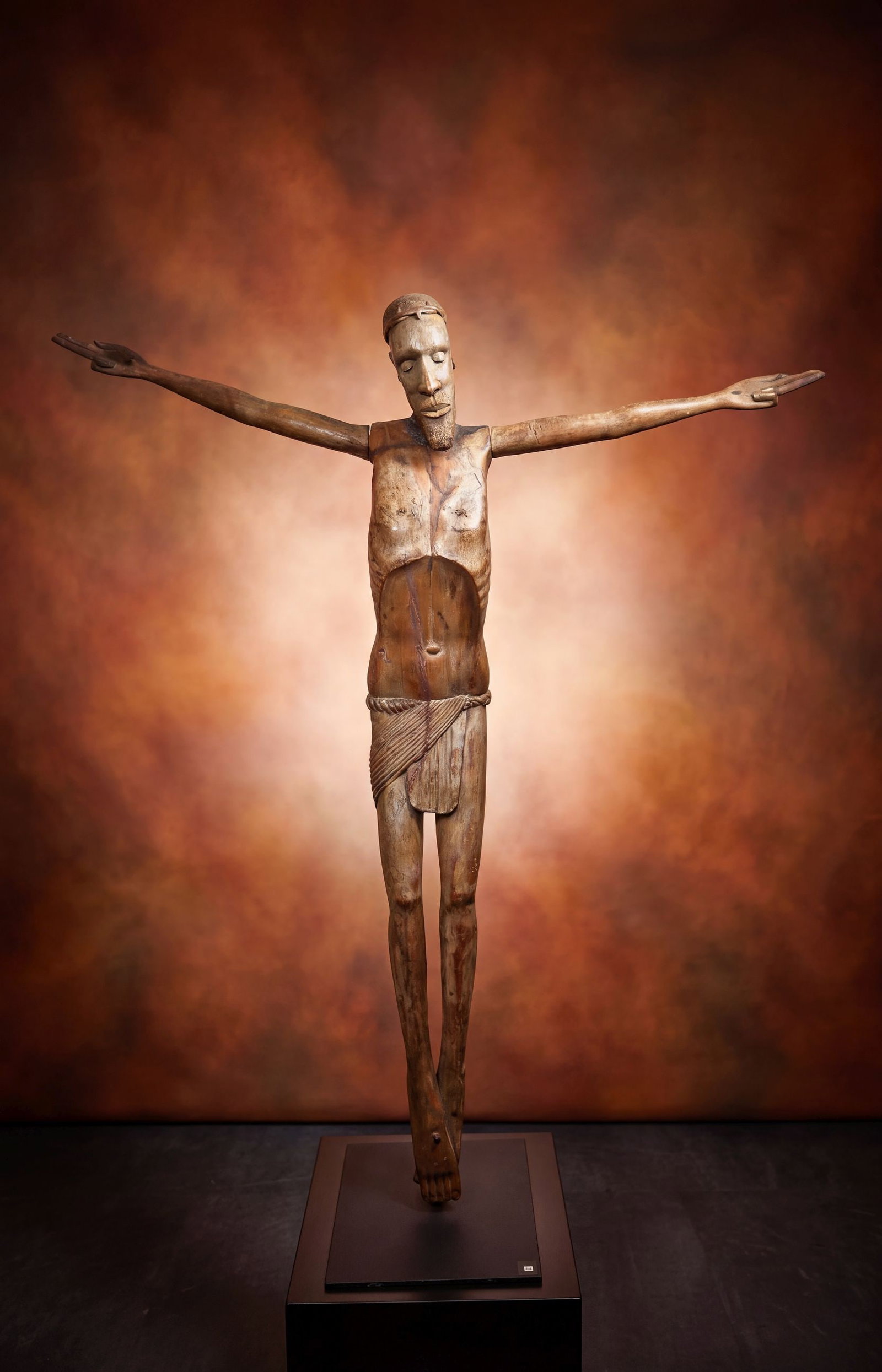 A Monumental Old Makonde Christ Sculpture: A tall carved wooden effigy of Christ as seen on the cross, with hands outstretched and nails in his palms and feet, his head wears a crown of thorns and is tilted slightly of axis, his eyes closed an