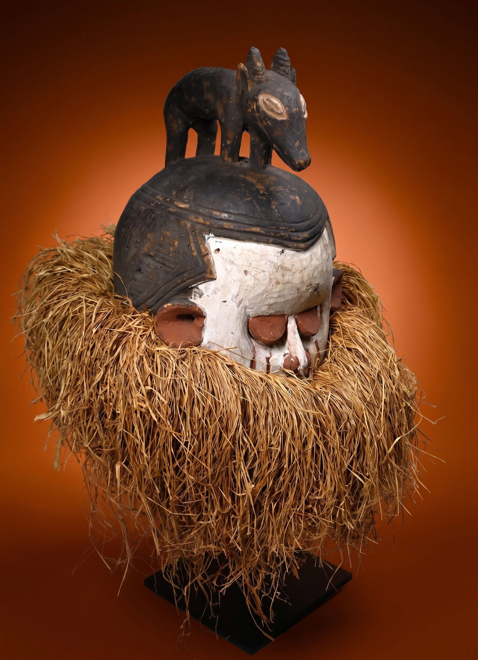A Fine Suku Helmet African Mask: a carved wooden helmet mask carved with an oval face, slit eyes under arched lids, slender triangular nose and painted scar designs. The coiffure rises to a central crest featuring a zoomorphic