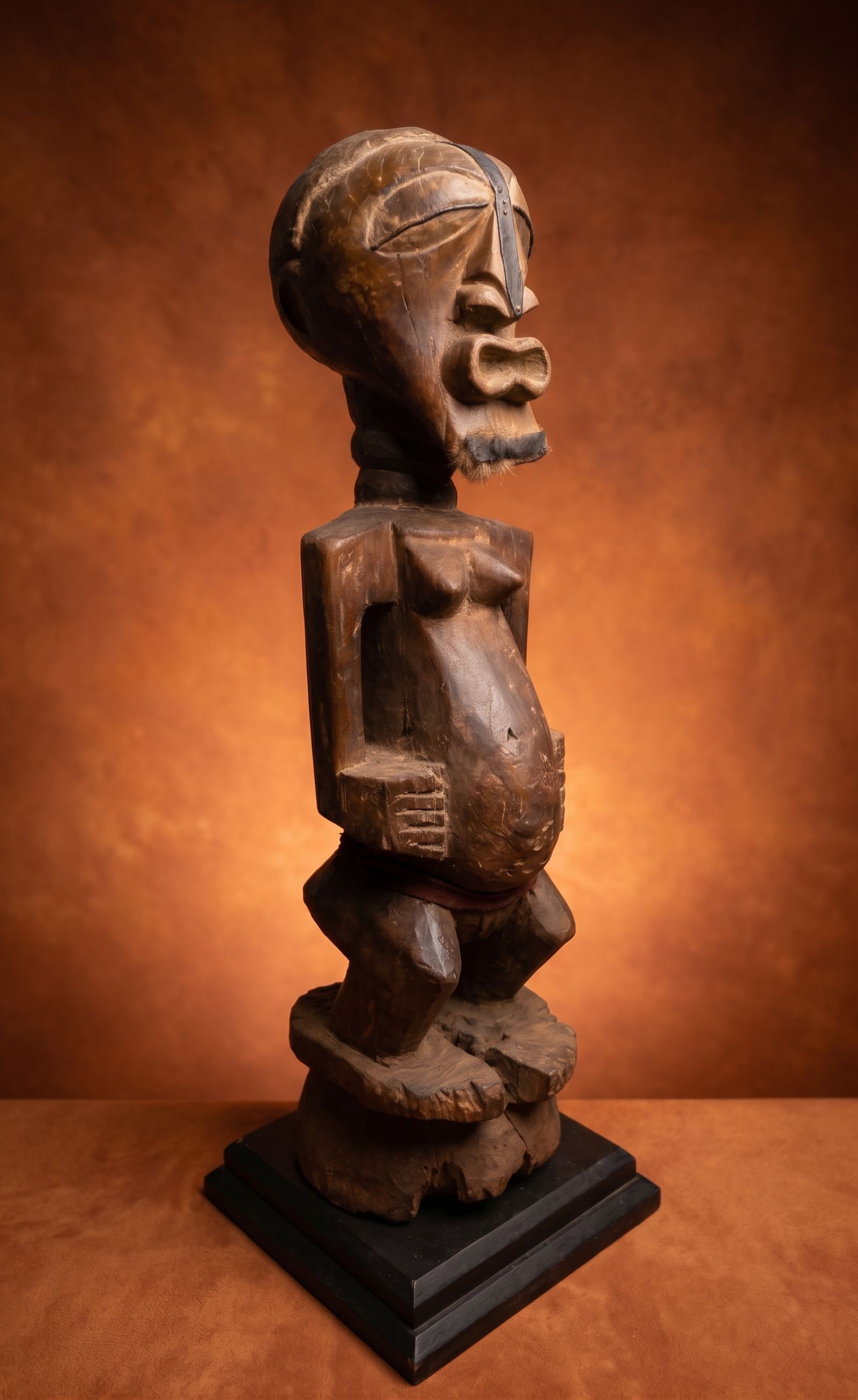 A Songye Nkisi Power Figure: This is a tall carved wooden effigy with classic facial features, embellished with hammered iron strips and remains of animal hide. This Songye nkisi (or nkishi) is a powerful protective sculpture fro