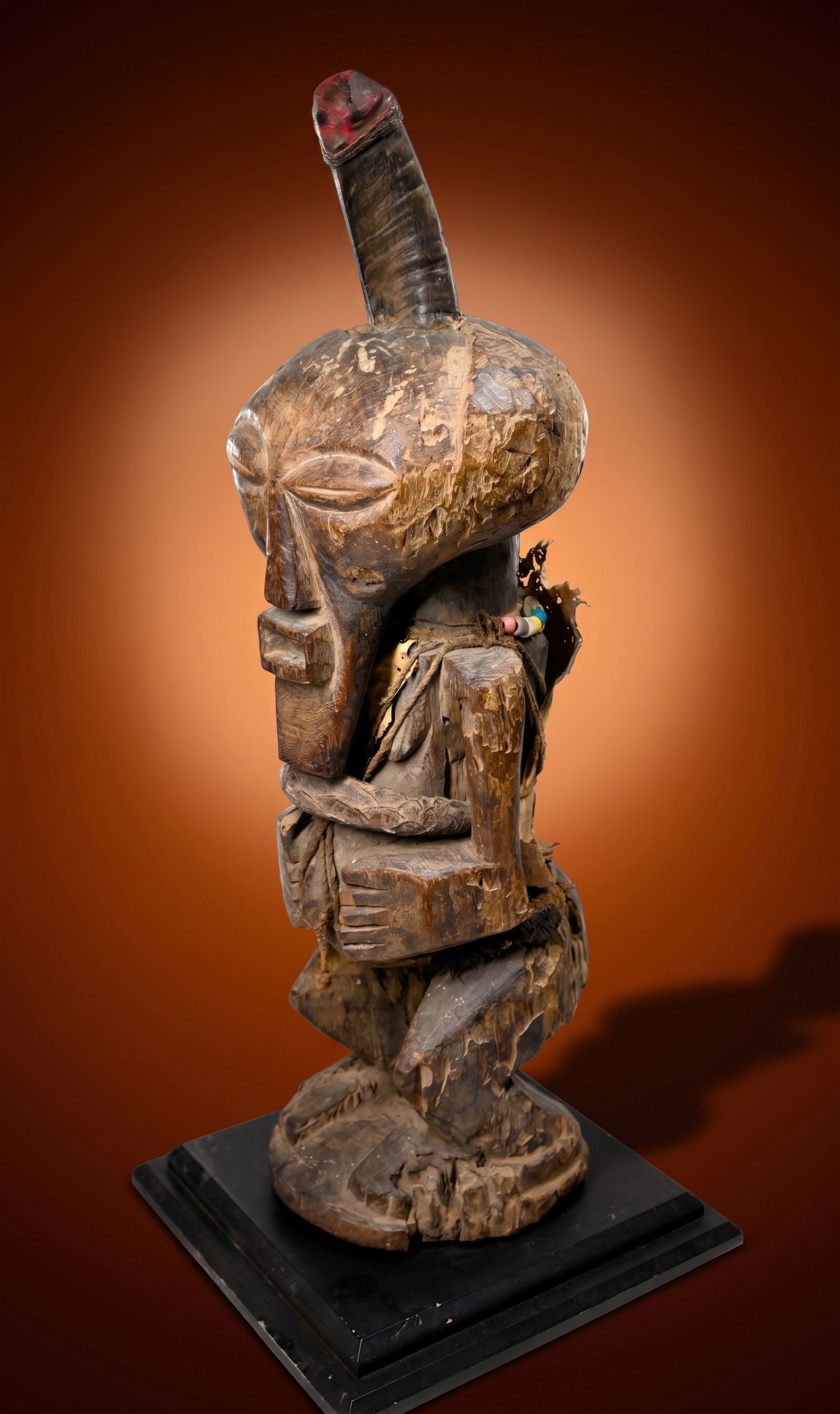 A Songye Magic Fetish Shrine Idol: This is a highly stylized carved wooden fetish idol with classic facial features, embellished with animal hide, textiles, old glass beads and the central horn has been modified to appear as a phallus 