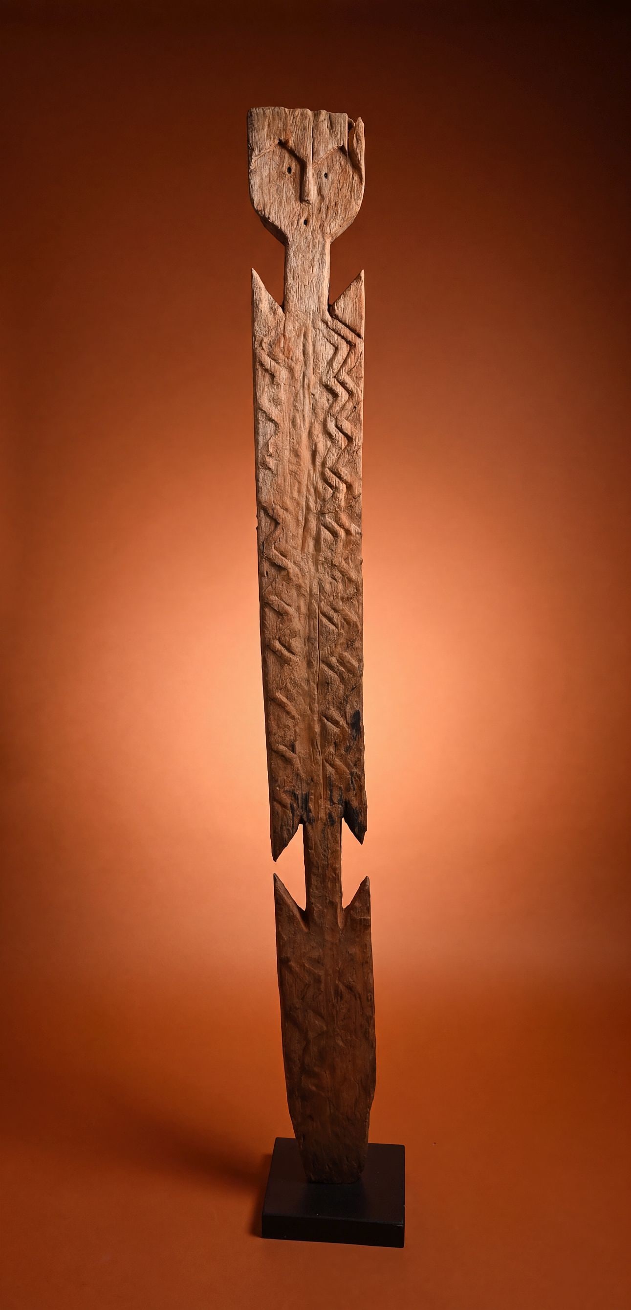 Giriama Veneration Post Kigango: A Carved wooden marker post with linear and geometric designs, and a faded face on top. The Giryama people of the Kenyan coast are known for their long-standing tradition of carved wooden marker posts