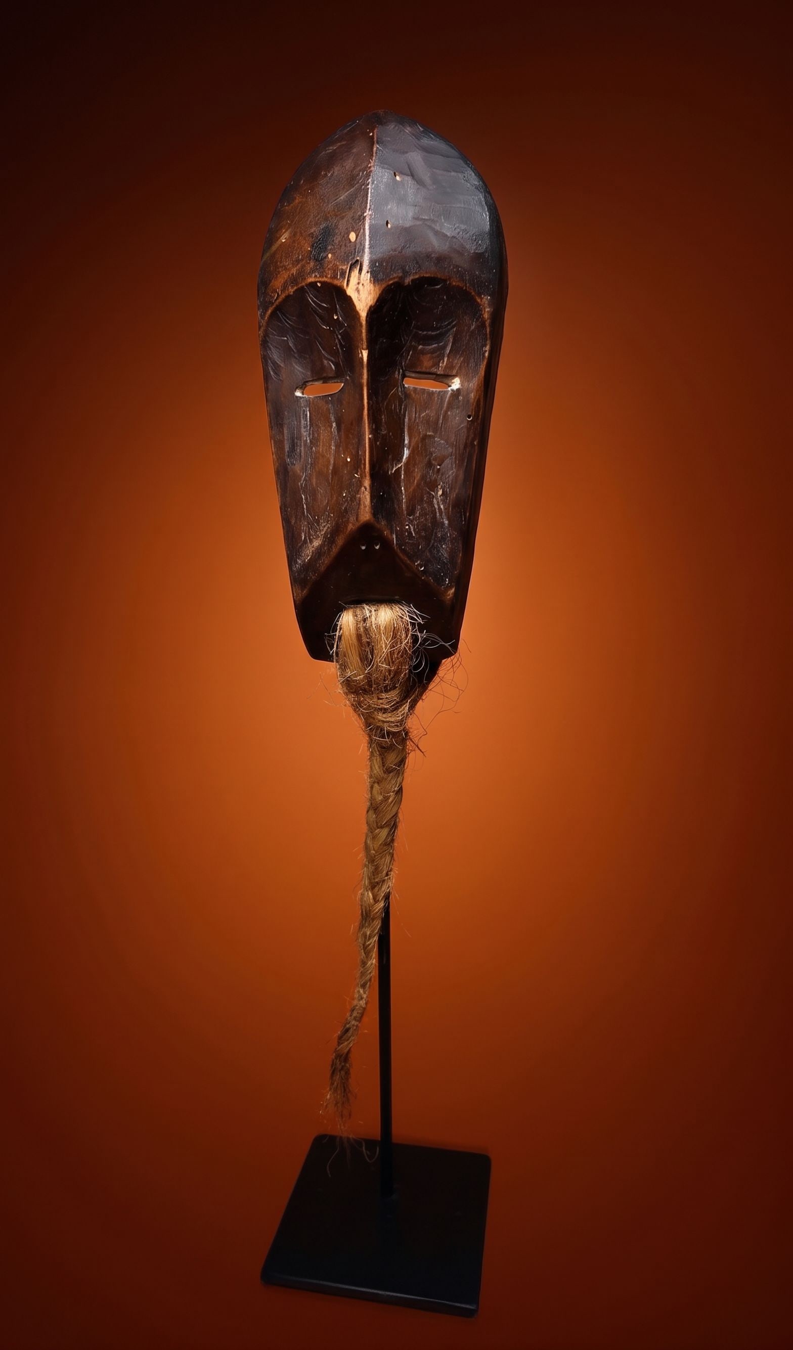 A Lega Lukakwongo Mask: A carved wooden diminutive mask with geometric form and long braided rope beard. The Lega Bwami society would create such masks to hang as clan totems and wear during ceremonies, often on their arms a