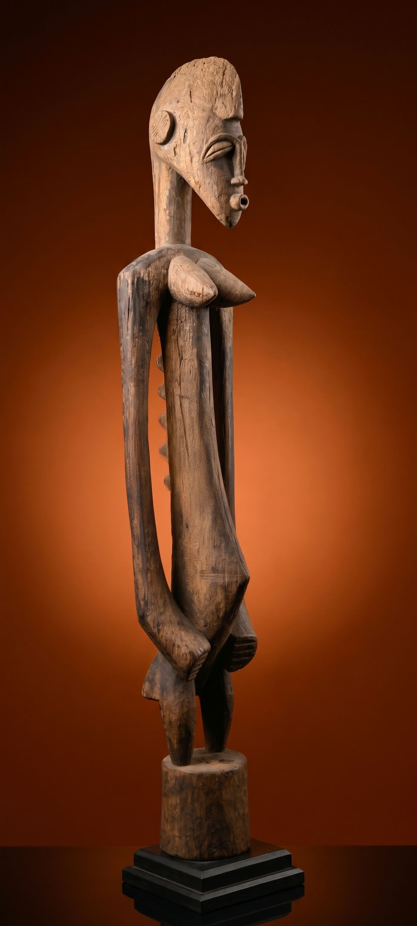 A Senufo Madeo Female Sculpture: A carved wooden female Madeo or ambivalent spirit altar figure that is similar to a deble sculpture. This figure has a well weathered surface and a unusual raised reptile like design on her back. The 