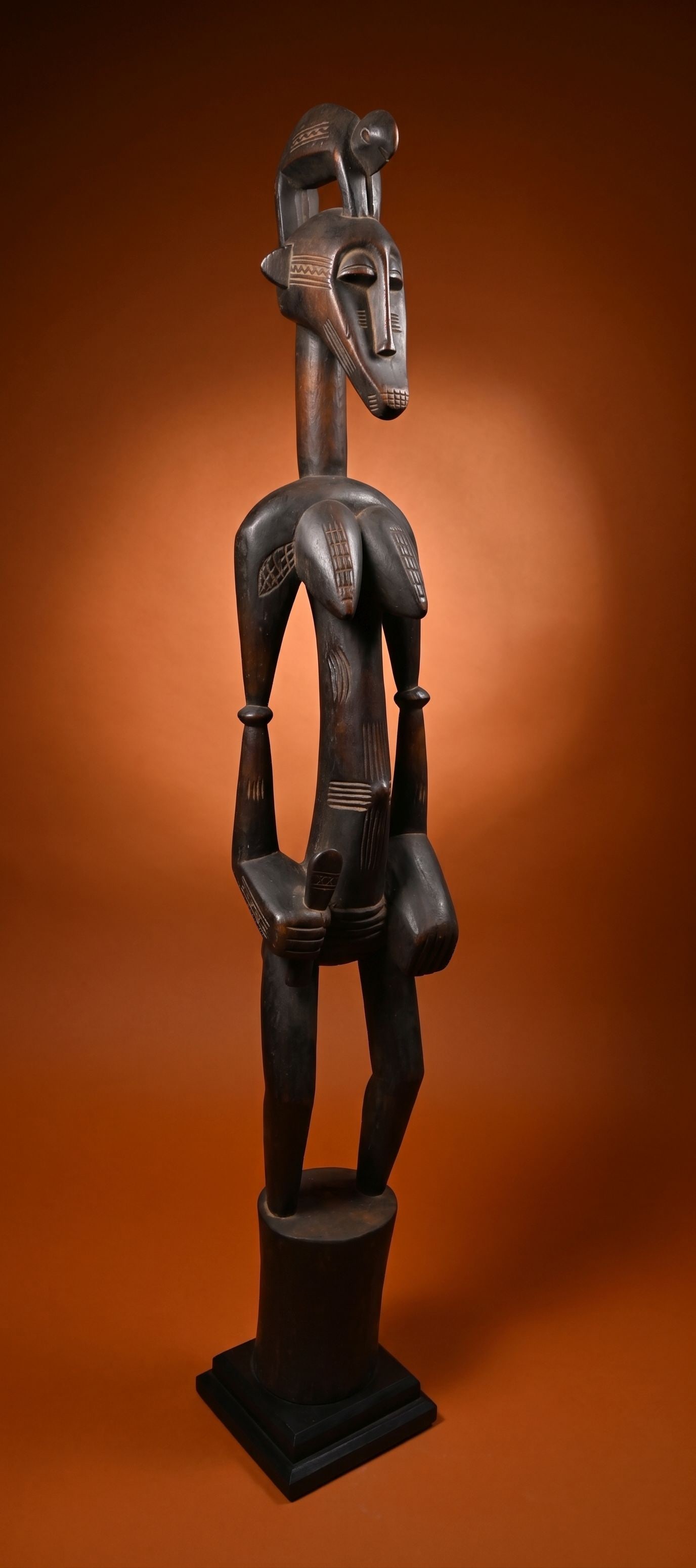 A Tall Senufo Deble with Chameleon On top: A carved wooden female deble sculpture with a highly stylized form, incised and raised designs and a wonderful chameleon effigy on top. This figure has a well handled and polished surface and measures