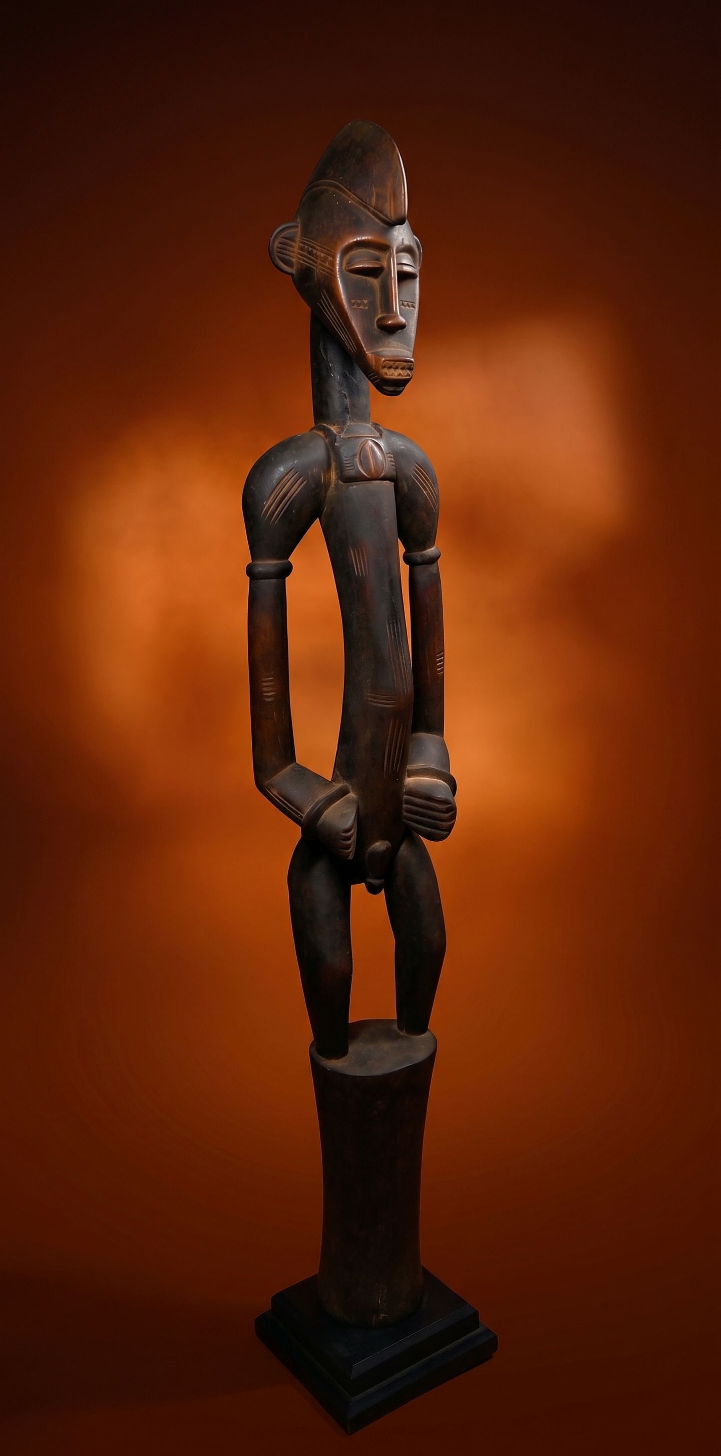 A Senufo Male Deble Sculpture: A carved wooden male deble sculpture with a highly stylized form, incised and raised designs and a wonderful carved cowrie shell medallion on his chest. This figure has a well handled and polished sur