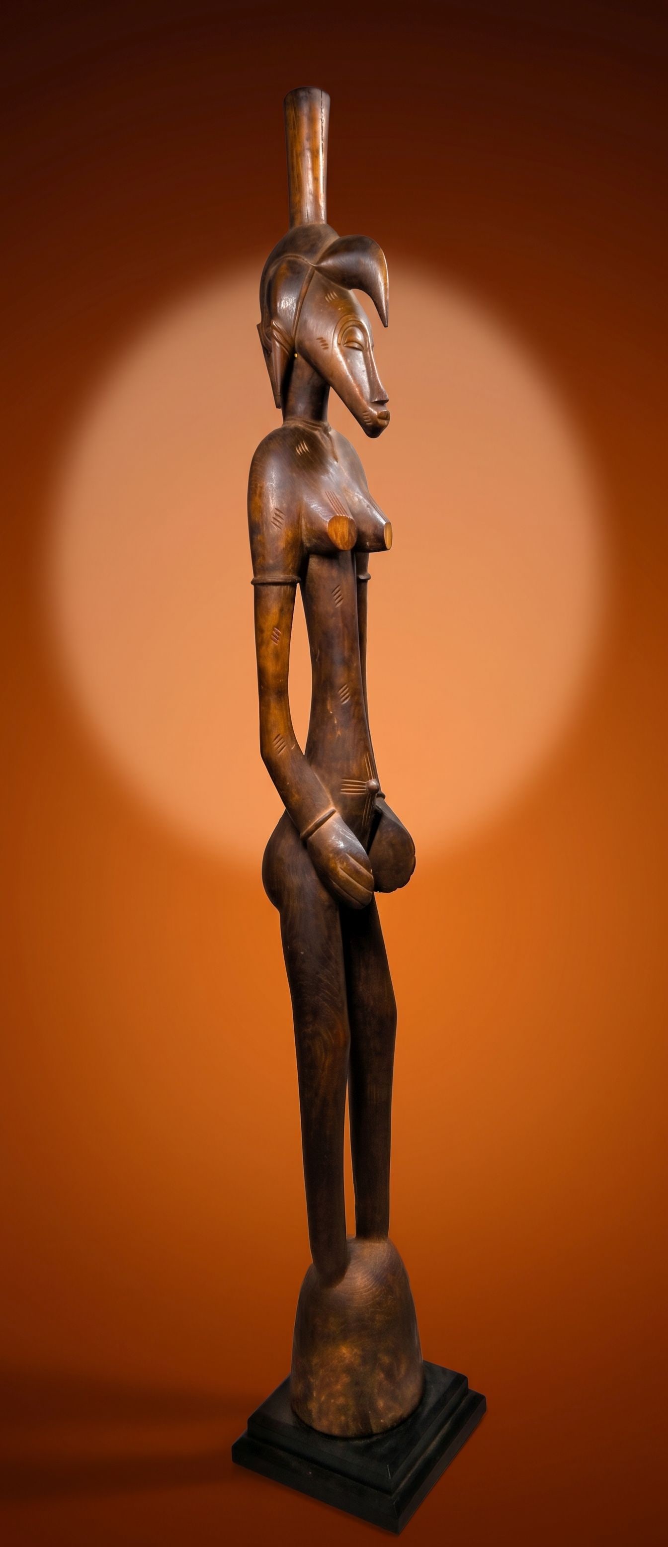 A Senufo Female Deble Sculpture: A very tall carved wooden female deble or rhythm pounder sculpture with a highly stylized form, incised and raised designs and a wonderful stylized face. This figure has a well handled and polished su