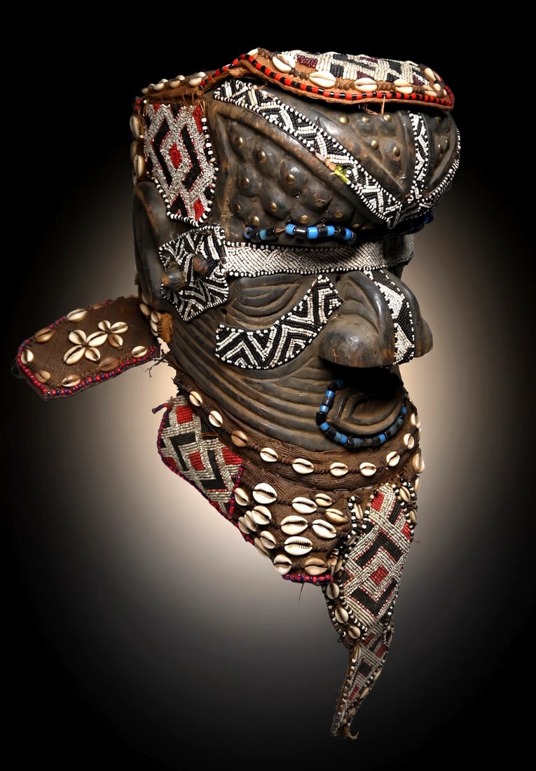 A Kuba Bwoom Helmet Mask: Carved wood and embellished with numerous layers of glass beads, shells and wonderful treatment to the face with carved ridges, bumps and lines. The mask has various incised designs creating a spectac