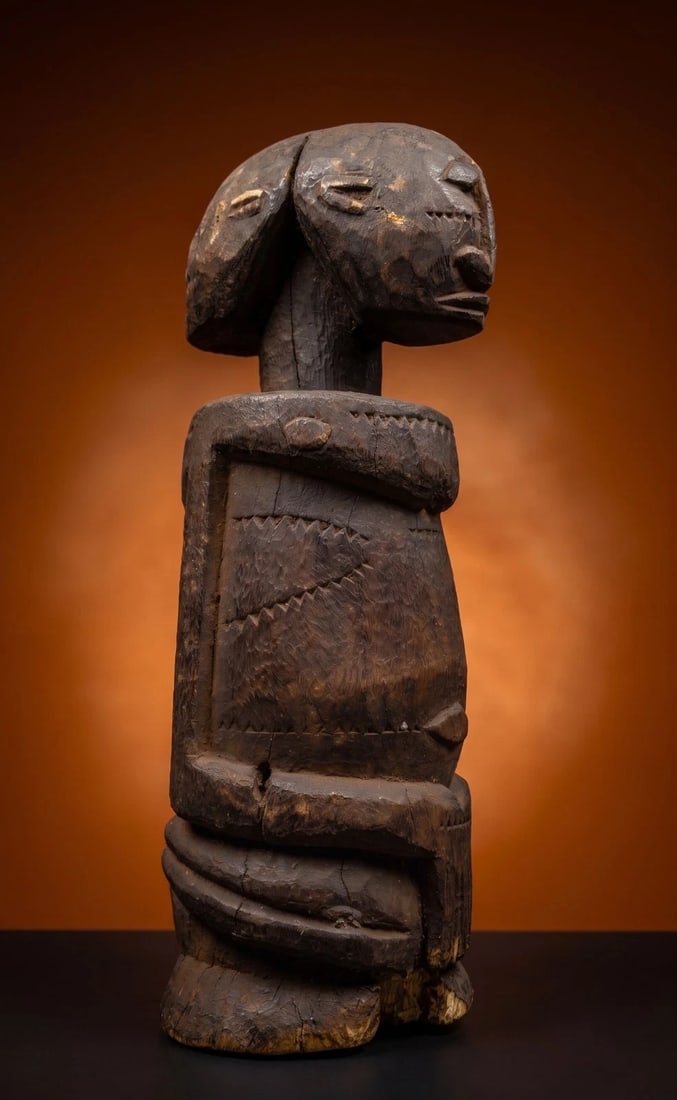 A Janus Dogon Sculpture: A Contemporary carved wooden janus form effigy of a stylized couple with male and female Janus head on cylindrical torso with minimalist arms and incised details. Dogon peoples, Mali, West Africa. The