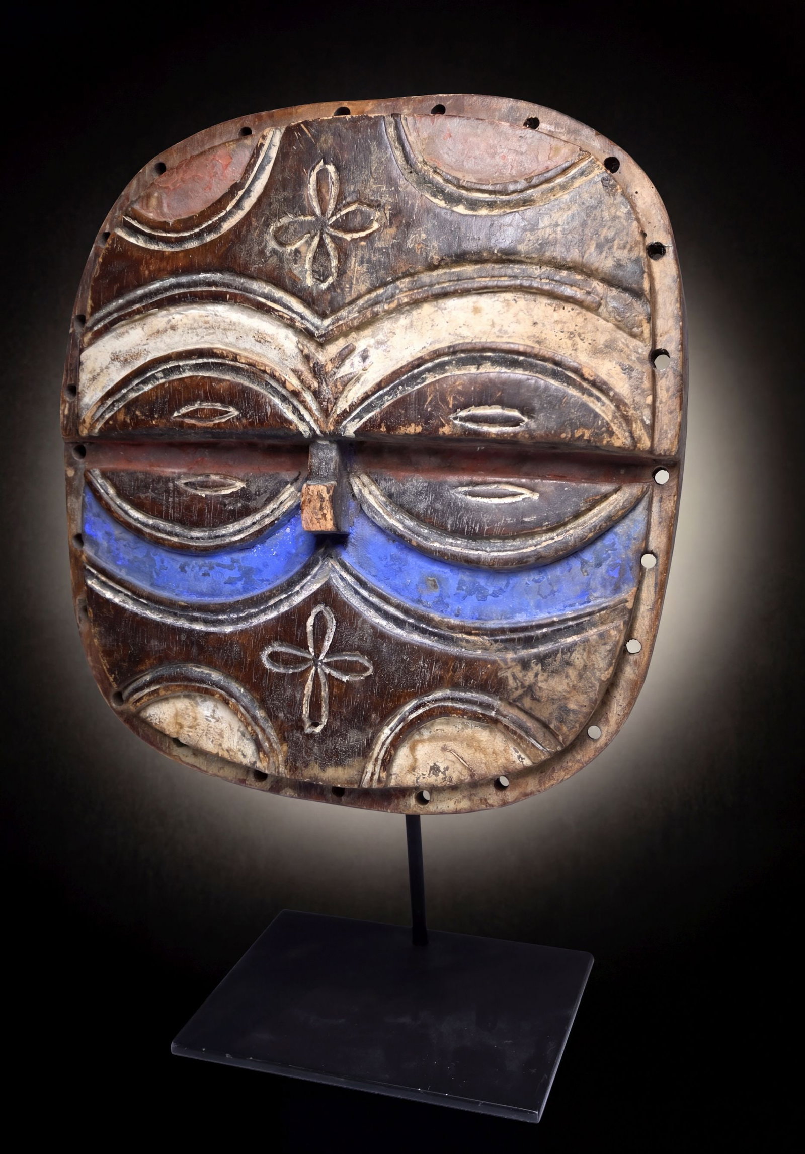 Vintage Teke Kidumu Mask: A carved wooden abstract mask known as a Kidumu with raised linear designs and painted with red, white and blue mineral pigments. The mask shows some actual age and handling, however how much it was e