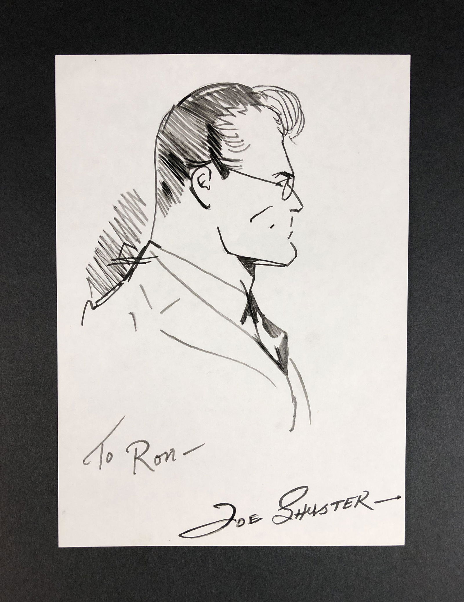 Joe Shuster - Ink on Paper (style of): This lot consists of an ink illustration on paper, done in the distinctive cartoon style of Bob Kane (American, 1915-1998). A hand inscription at bottom reads, "To Ron -- Joe Shuster." Image depicts a