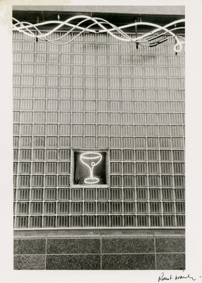 NEON COCKTAIL GLASS, by ROBERT FRANK: NEON COCKTAIL GLASS, by Robert Frank. 13 7/8 x 11- inch gelatin silver print, ca. 1955, signed recto. Curious play of curved neon designs against a rigid grid of squares. The scale can't be easily de